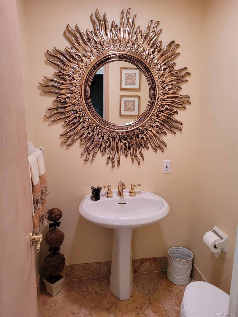 Elegant powder room featuring a pedestal sink with brass faucet, decorative sunburst mirror with gilt finish, tile flooring, and soft neutral wall ton