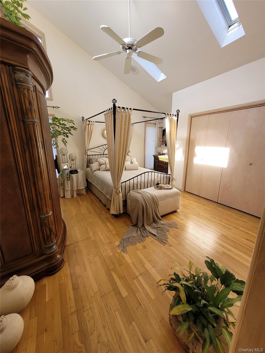 Vaulted ceiling with skylight, wood-finish flooring, ceiling fan, and built-in closet with bifold doors