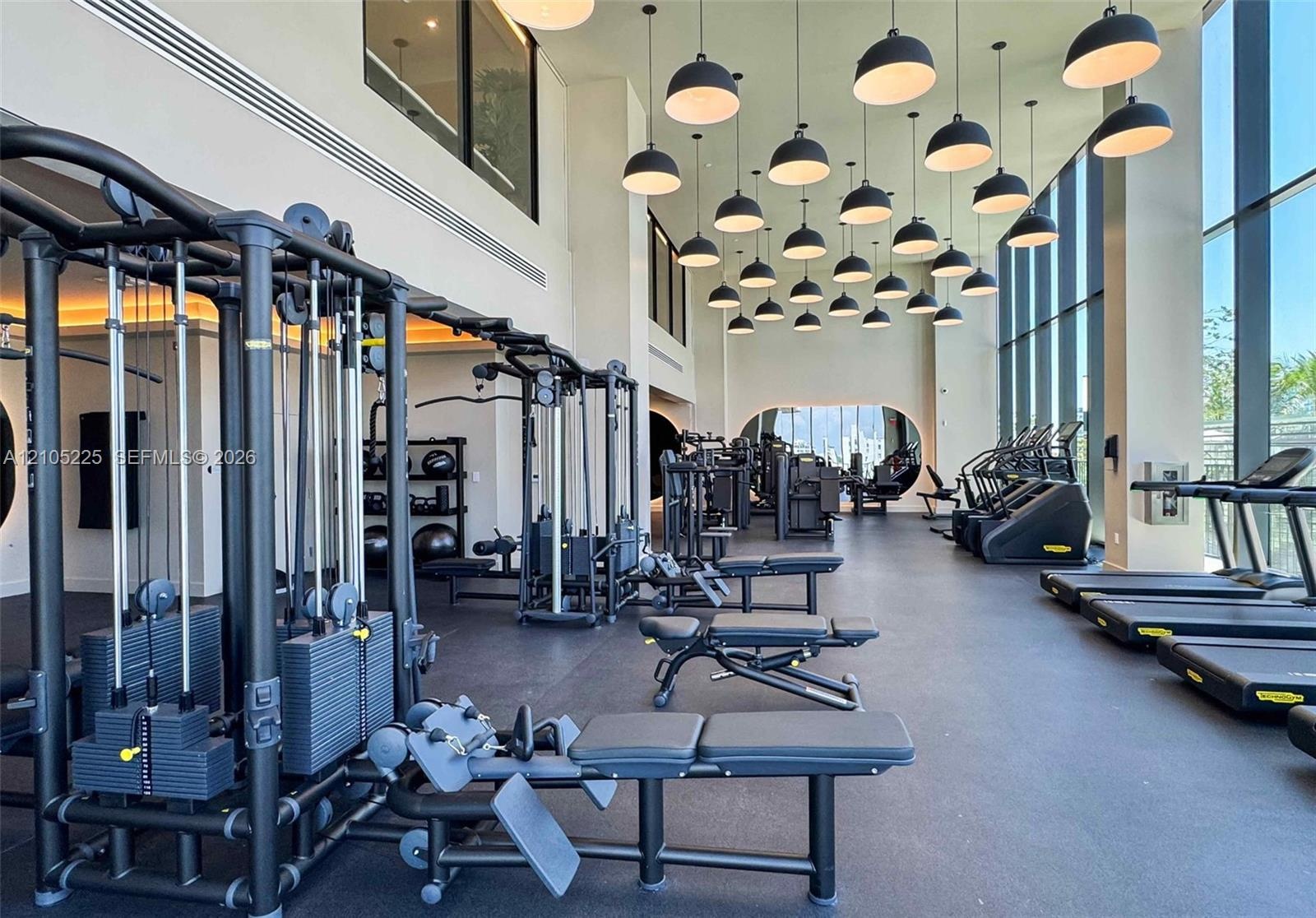 Fitness center featuring a high ceiling, extensive natural light from floor-to-ceiling windows, numerous pendant light fixtures, and varied exercise e