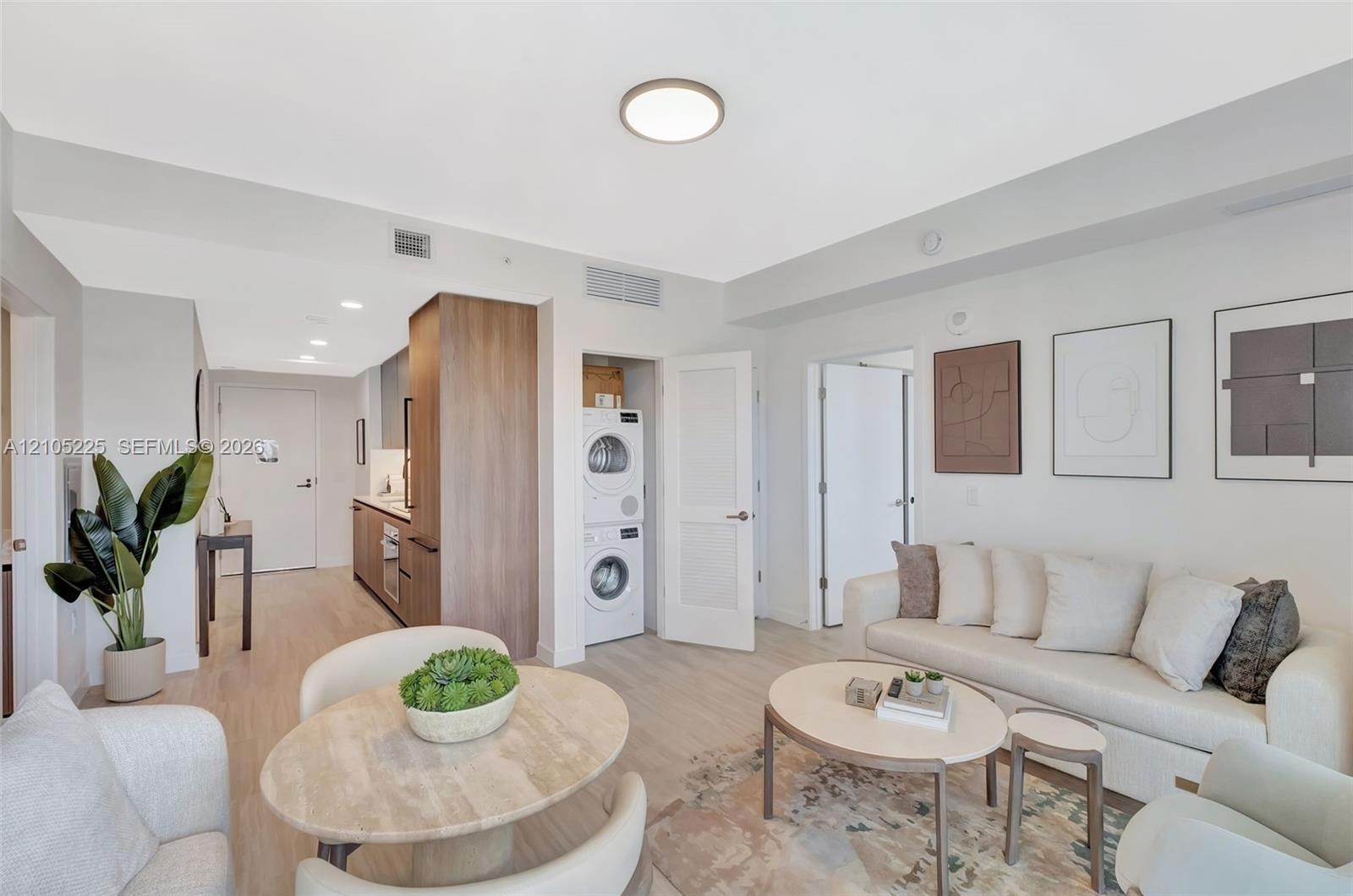 Open-concept living area with wood-finish flooring, recessed lighting, and a built-in stacked washer and dryer