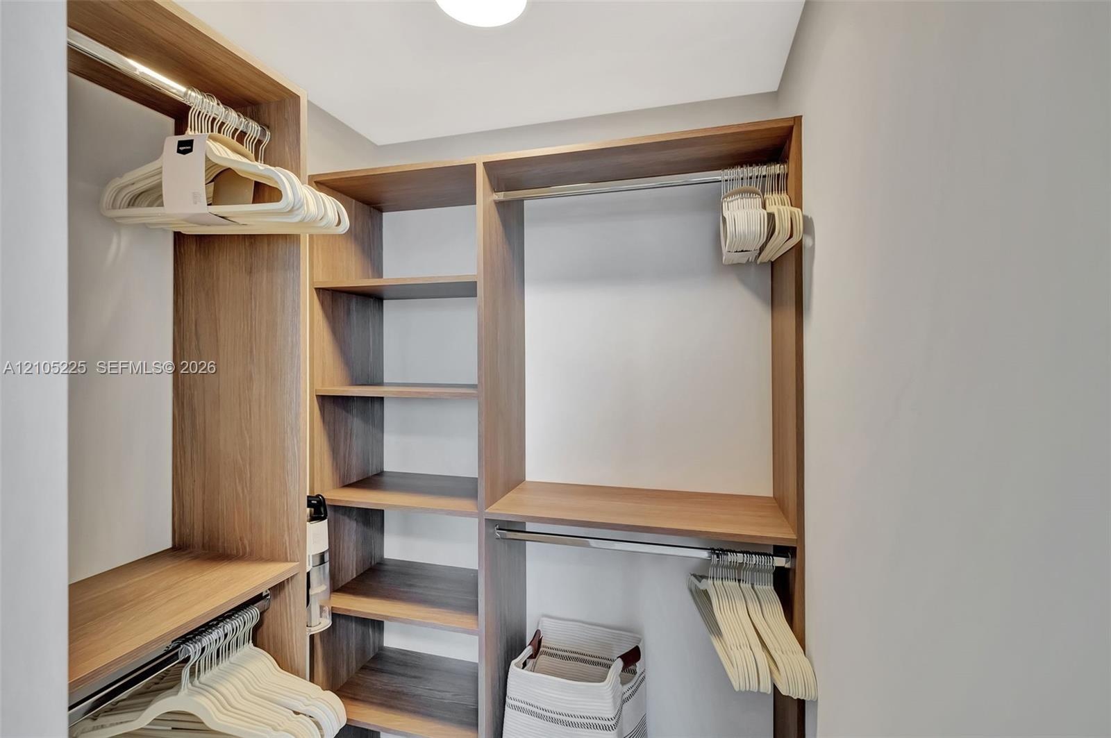 Walk-in closet featuring custom wood-finish built-in shelving, multiple hanging rods, and integrated overhead storage