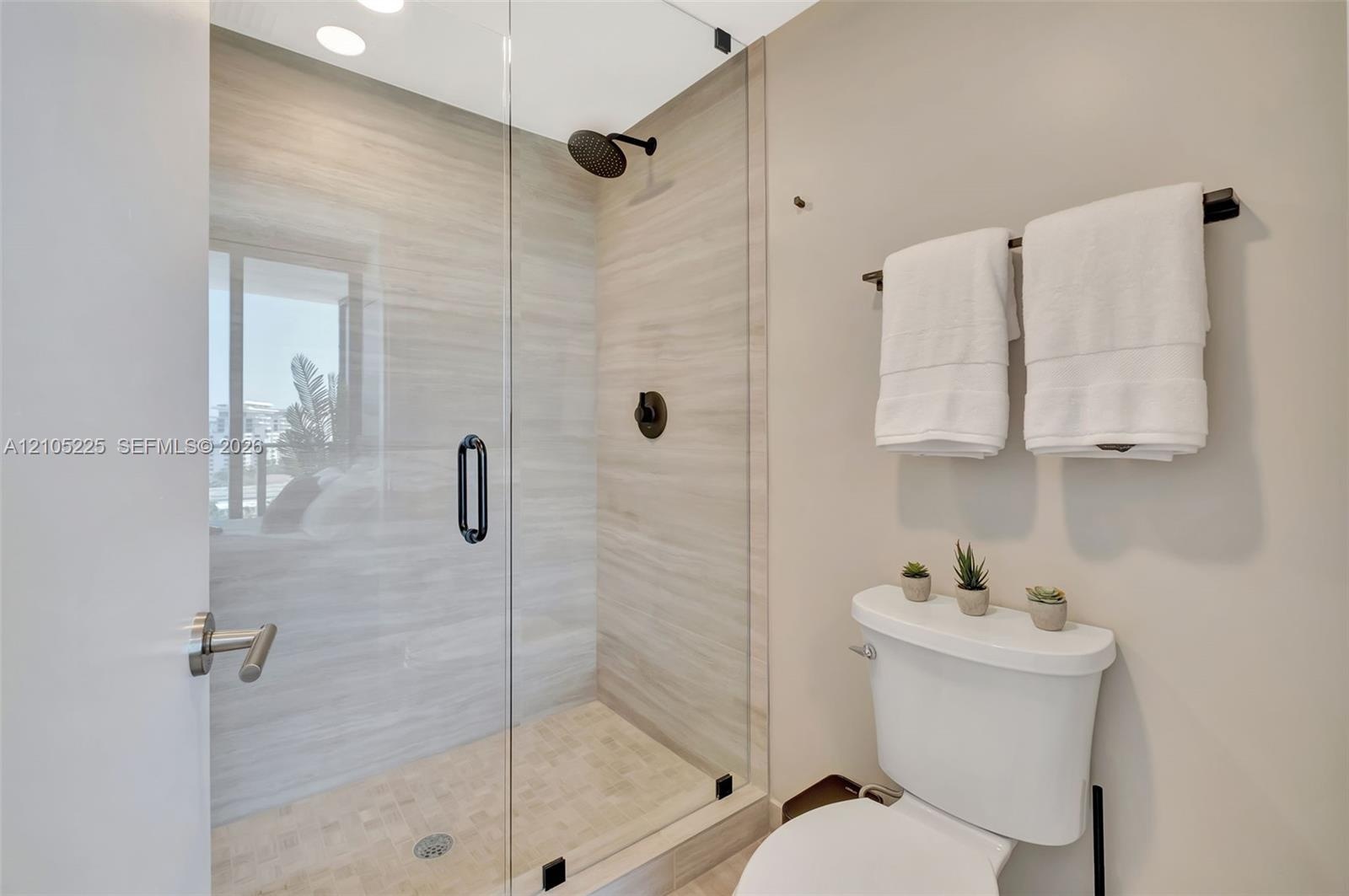 Walk-in shower featuring a frameless glass enclosure, horizontal stone-finish tile surround, textured stone-finish floor tile, and matte black plumbin