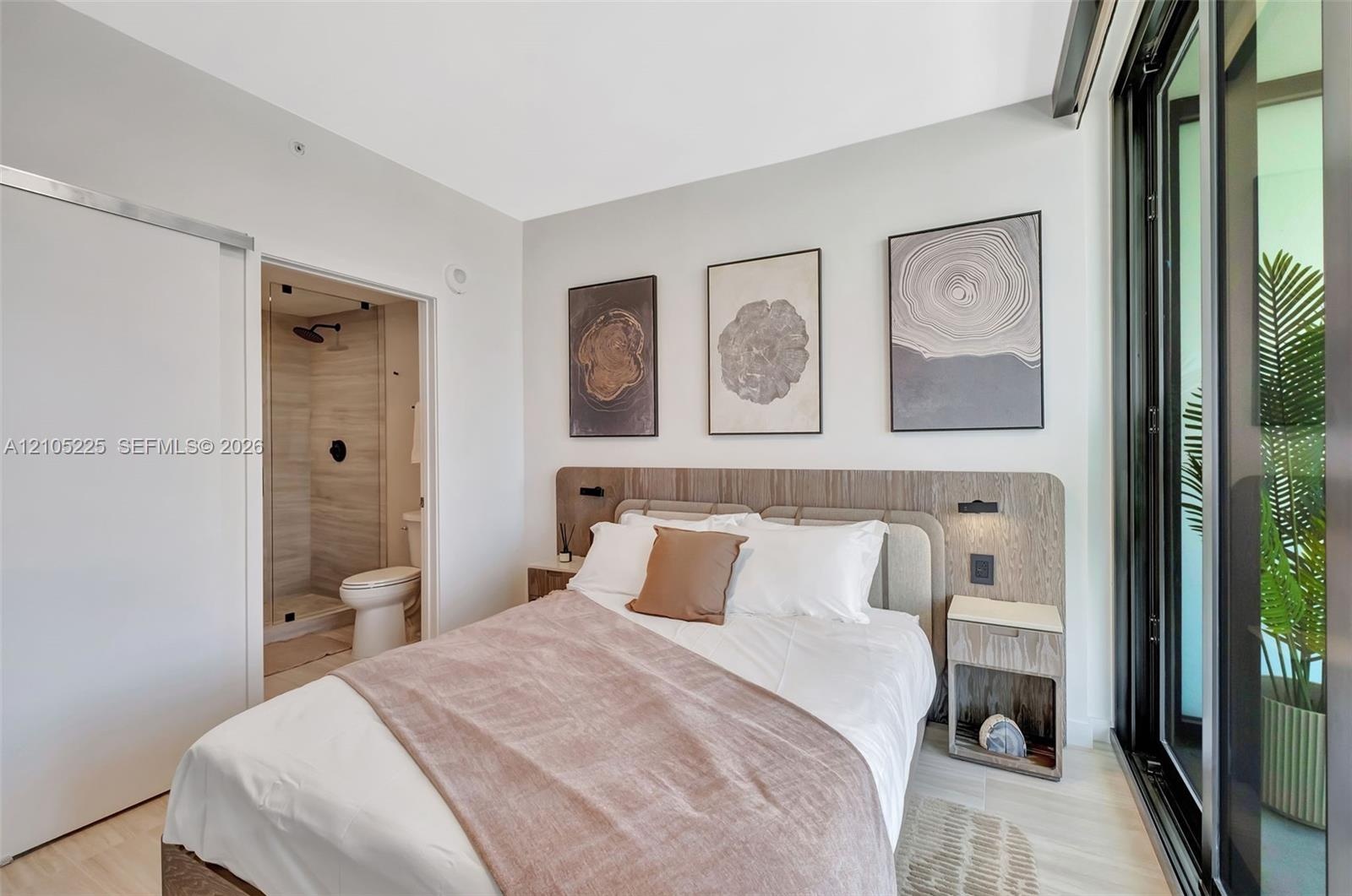 Light wood-finish flooring, built-in headboard with integrated lighting, attached nightstands, and a full-height sliding glass door