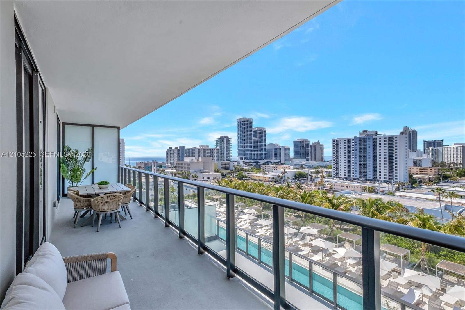 Covered balcony featuring concrete flooring, a glass and metal railing system, and city skyline scenery