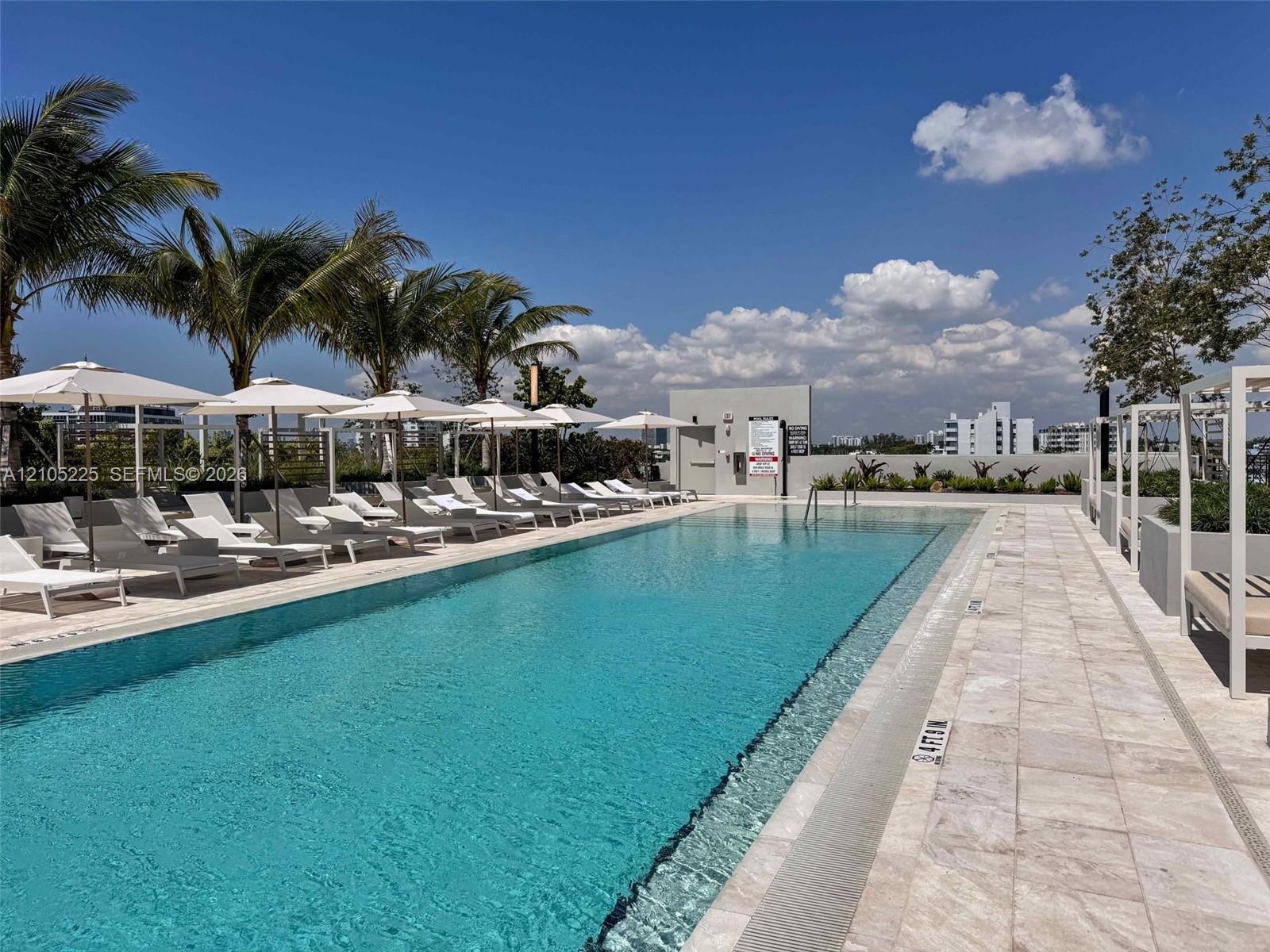 Expansive swimming pool with integrated lounge areas and sun umbrellas, bordered by tropical landscaping and a tiled deck