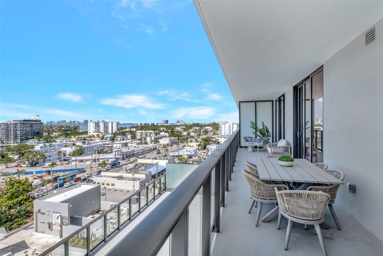 Expansive balcony with concrete flooring, glass panel railing, and multiple sliding glass doors