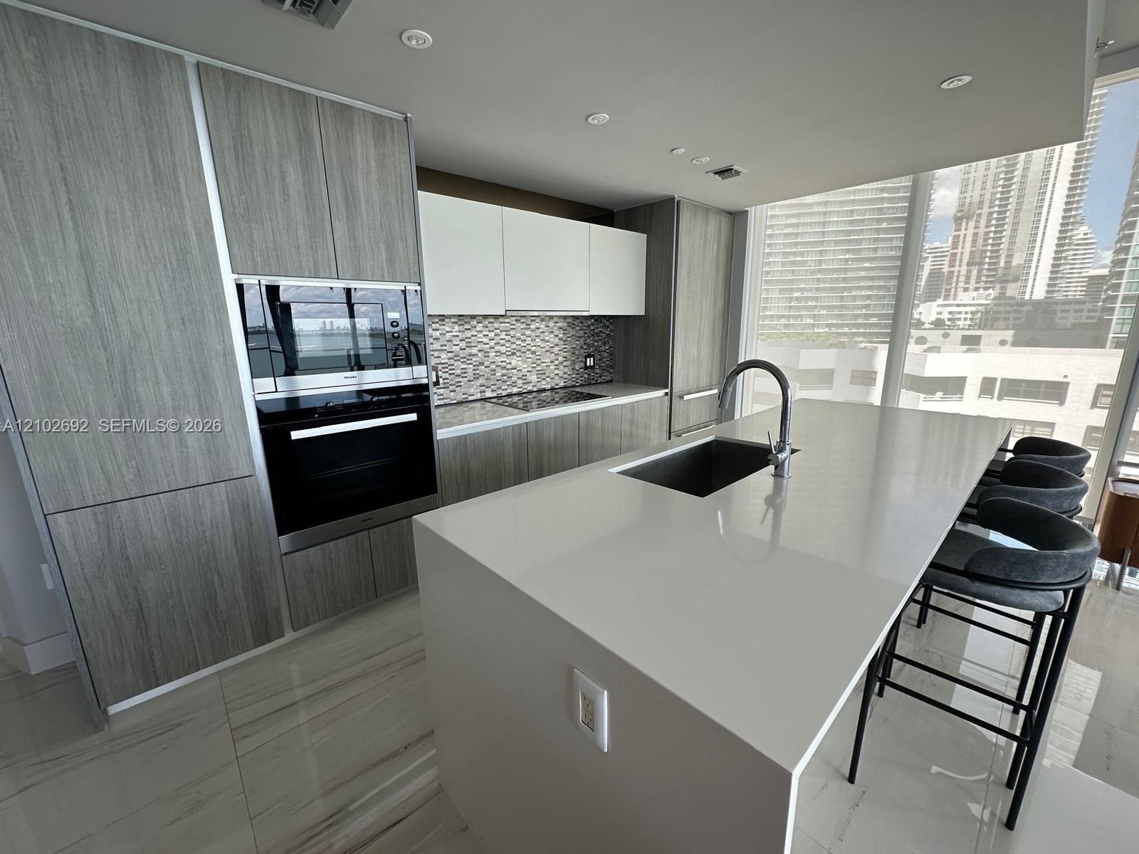 Kitchen featuring a central quartz-top island with an integrated sink, custom wood-finish cabinetry, built-in stainless steel appliances, and floor-to