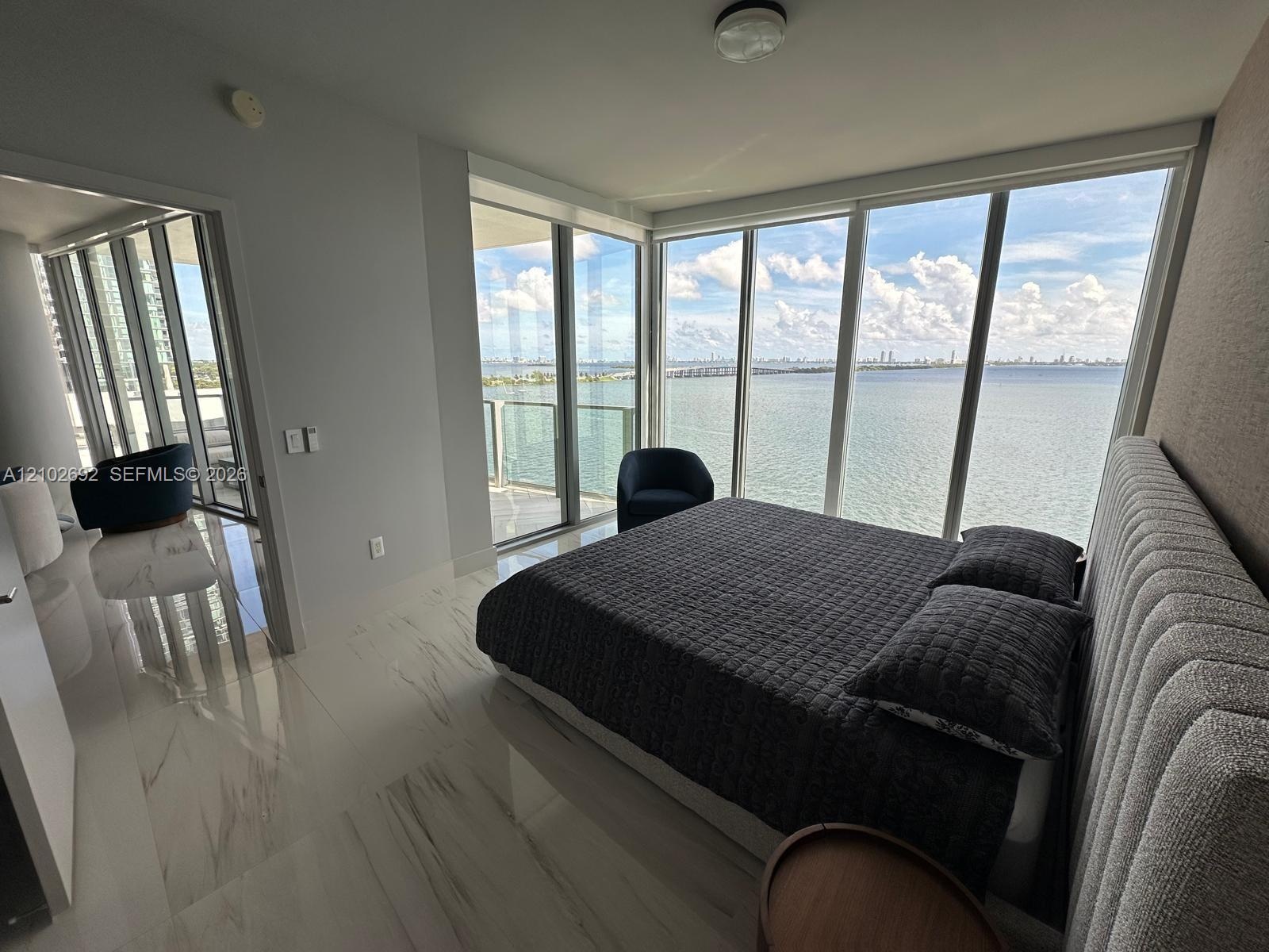 Floor-to-ceiling windows, polished stone-finish tile flooring, glass-railed balcony, and expansive water scenery