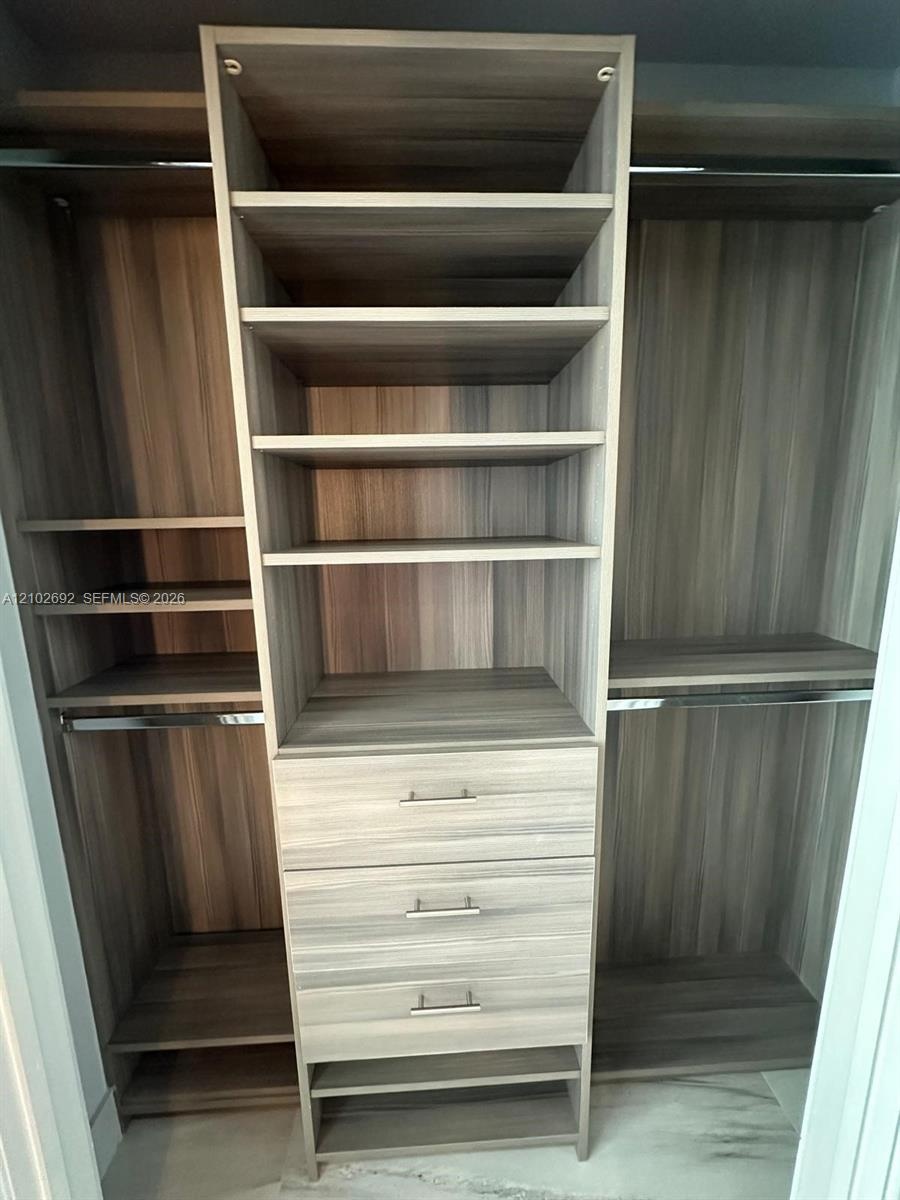 Custom storage system featuring wood-finish cabinetry, built-in shelving, three integrated drawers with metallic pulls, and stainless steel hanging ro