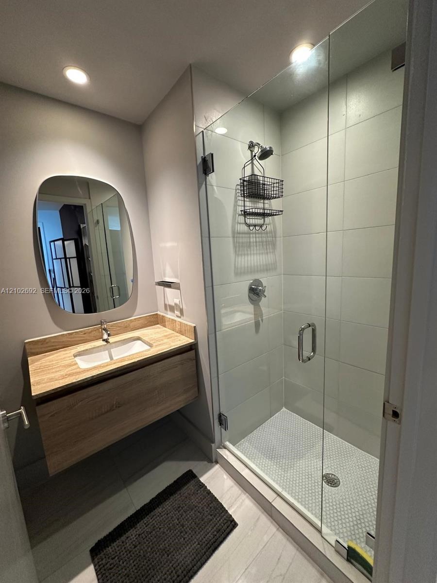 Floating vanity with wood-finish cabinetry, rectangular under-mount sink, frameless glass shower enclosure, and tiled shower surround with mosaic floo