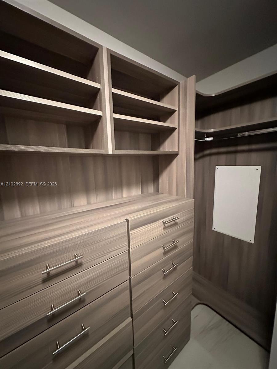 Built-in closet system featuring wood-finish cabinetry, multi-tier open shelving, integrated dresser drawers, brushed metal hardware, and a hanging ro