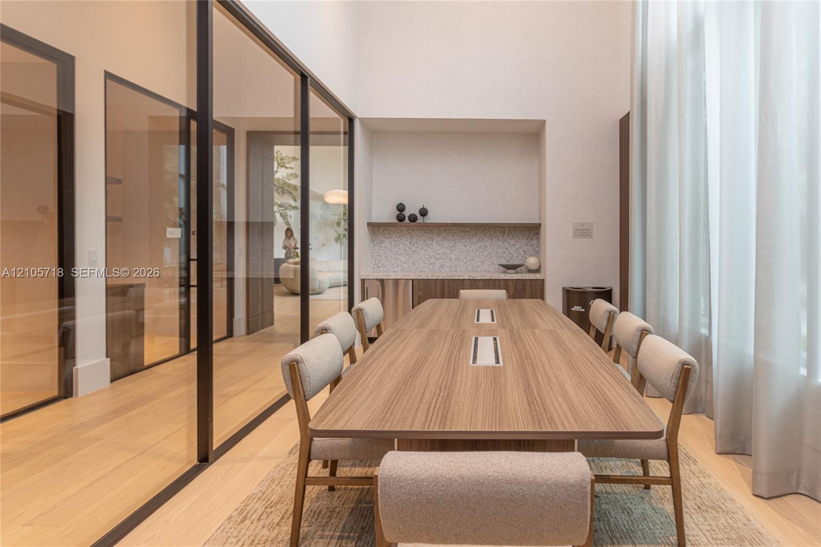 High-ceilinged room featuring expansive glass wall partitions with black metal frames, integrated built-in cabinetry with stone-surface counters, and 