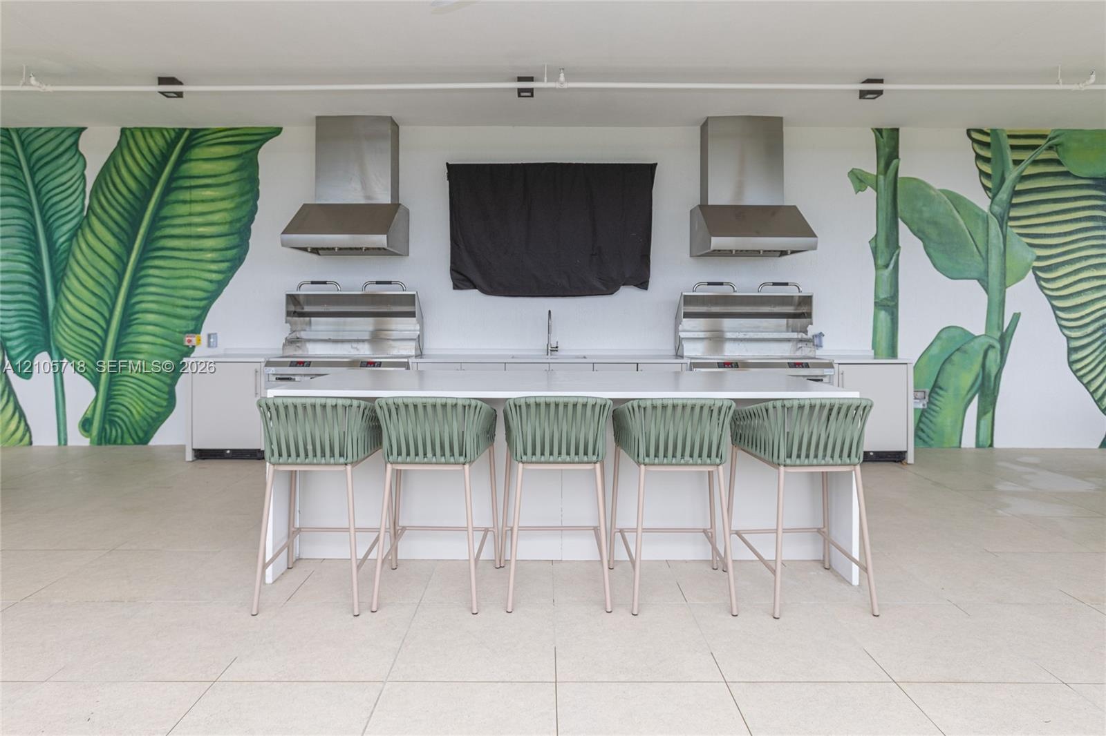 Outdoor kitchen featuring dual stainless steel grills, matching stainless steel range hoods, a central prep island with white countertop, and large-sc