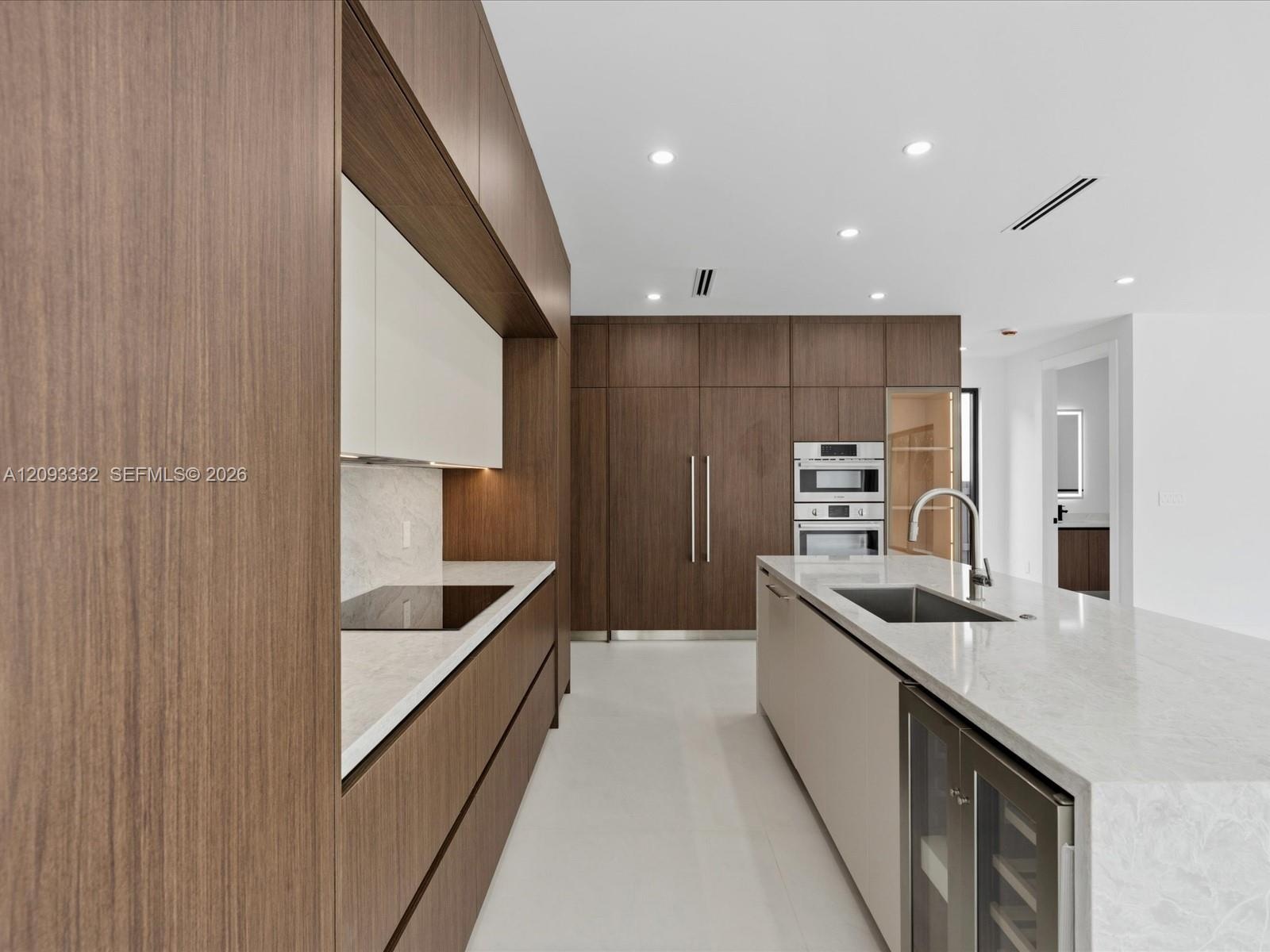 Modern kitchen featuring custom wood-finish cabinetry, stone-surface countertops, a large center island with integrated wine refrigeration, and stainl