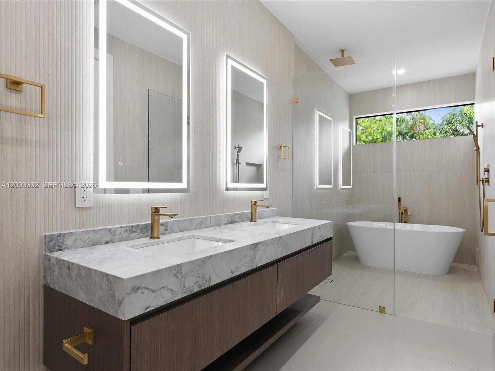 Floating dual-sink vanity with stone countertop, brass-finish fixtures, dual LED-backlit mirrors, freestanding soaking tub, and glass-enclosed walk-in