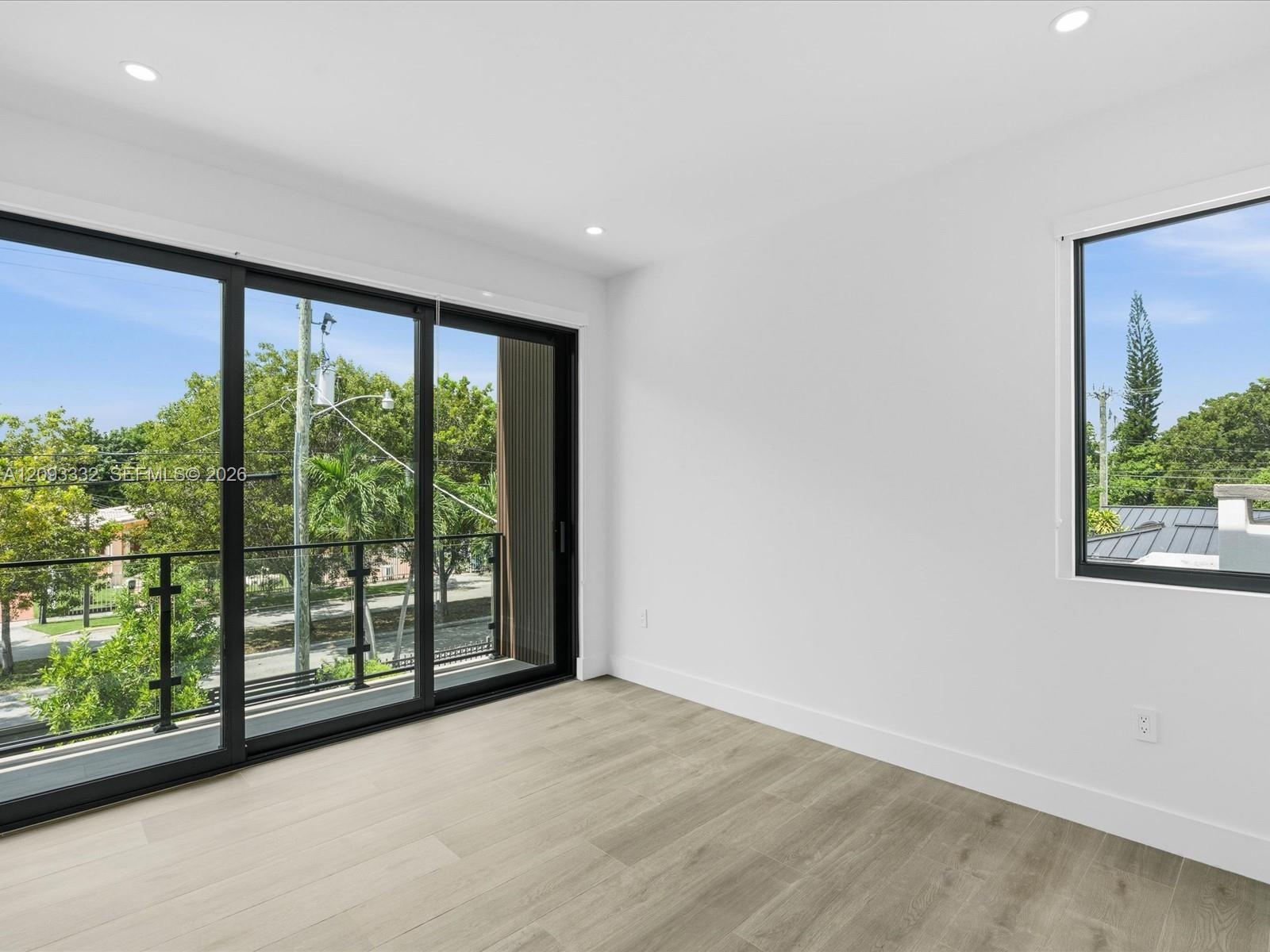 Room featuring wood-finish flooring, recessed lighting, expansive sliding glass doors, a private balcony with a metal railing, and large windows
