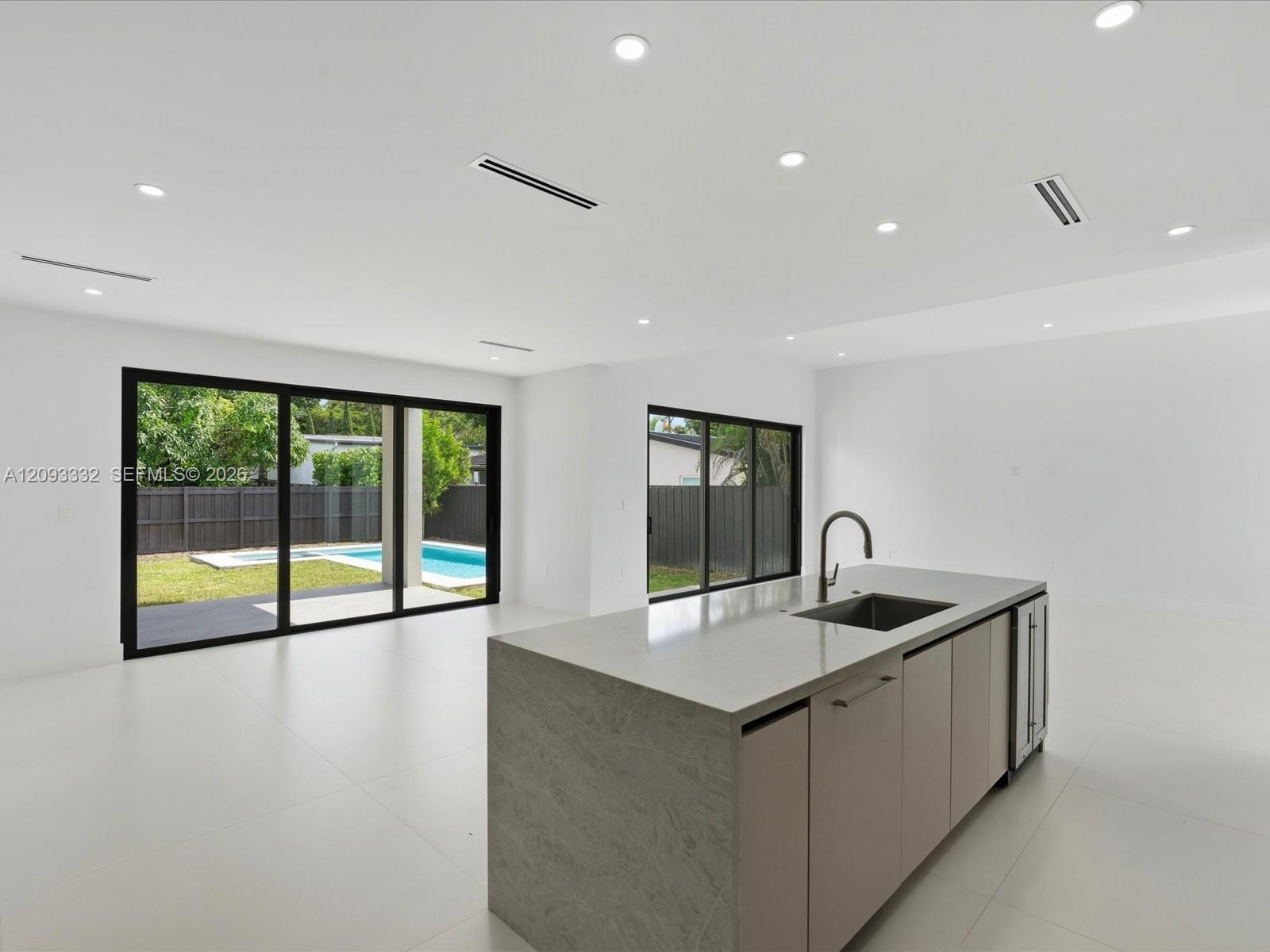 Open-concept interior featuring an expansive kitchen island with stone-finish countertops, undermount sink, and integrated beverage refrigeration
