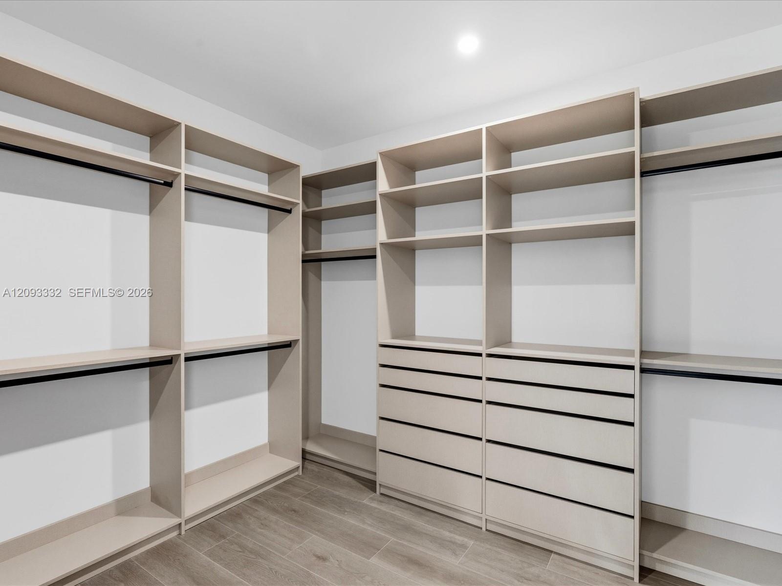 Walk-in closet featuring extensive built-in shelving, integrated hanging rods, a stack of custom storage drawers, and wood-finish flooring