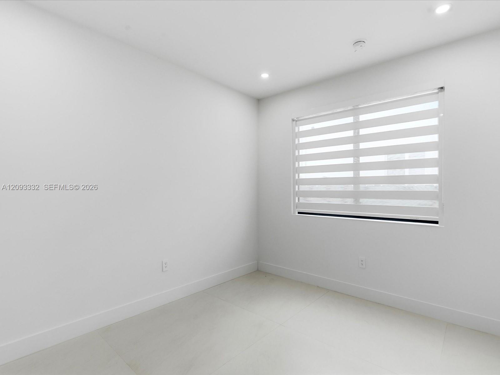 Neutral-toned interior space featuring large-format tile flooring, recessed lighting, and a window equipped with striped roller shades