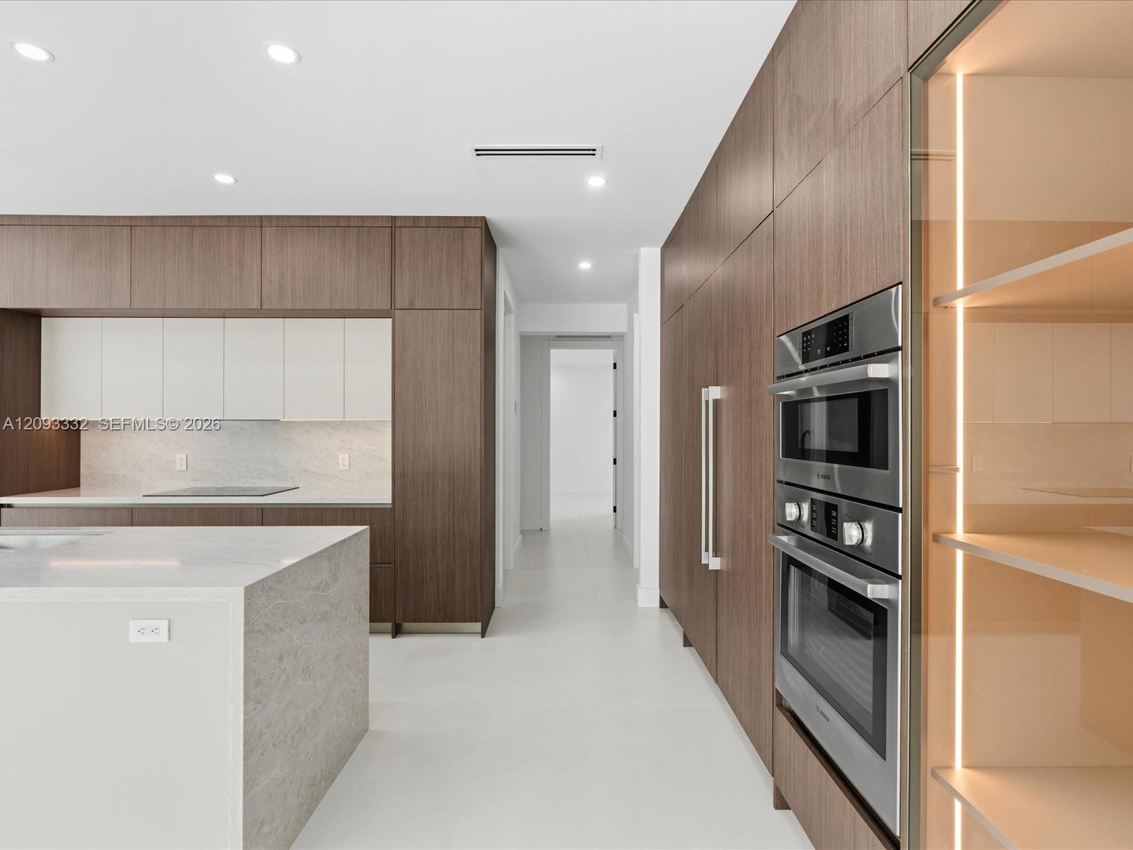 Modern kitchen featuring full-height wood-finish cabinetry, a stone-surfaced waterfall island, integrated stainless steel double wall ovens, and illum