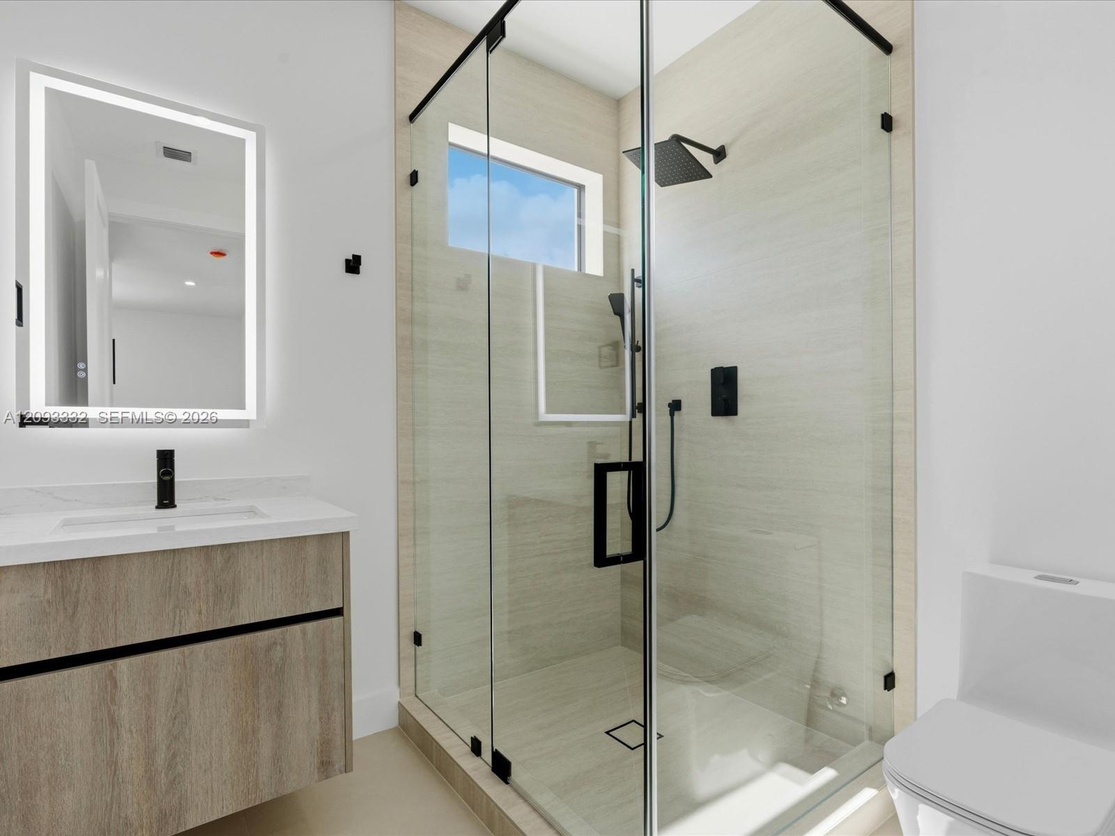 Bathroom featuring a floating wood-finish vanity, illuminated wall mirror, and walk-in shower with floor-to-ceiling tile, glass enclosure, and matte b