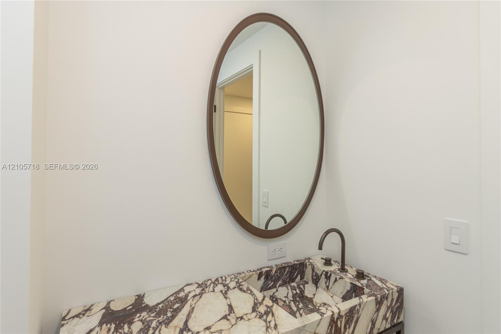 Stone countertop with an integrated basin, oval wall-mounted mirror with a bronze-toned frame, and a bronze-toned gooseneck faucet