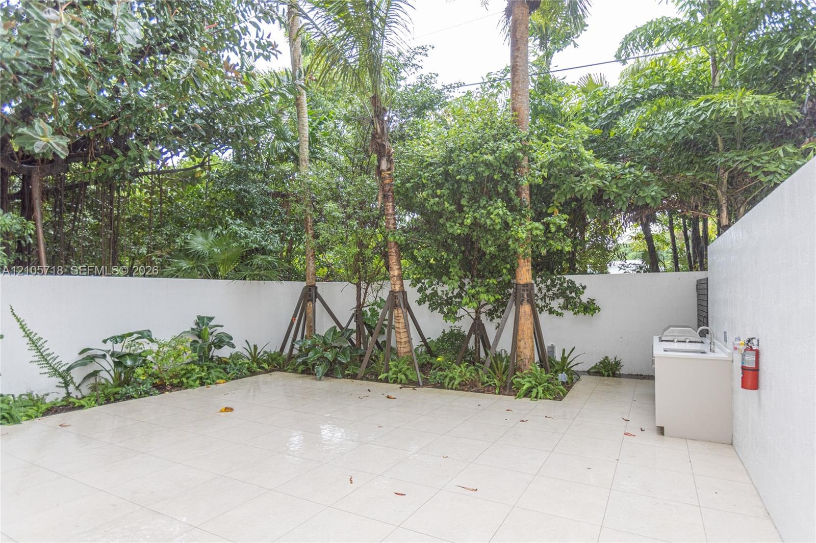 Outdoor courtyard featuring large-format tile flooring, built-in masonry counter with sink, solid perimeter wall, and established landscaping with mat