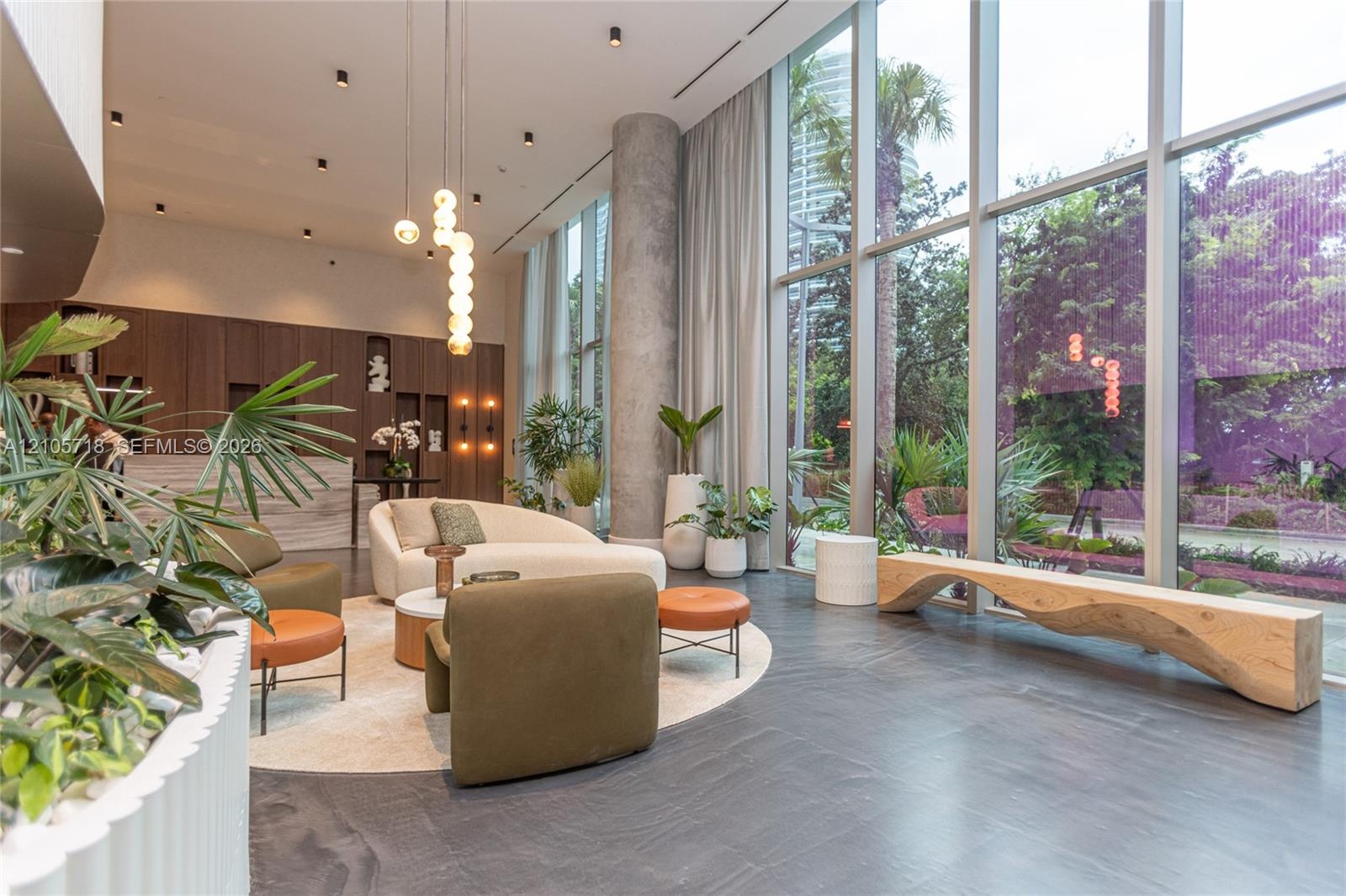 Double-height floor-to-ceiling windows, dark stone flooring, exposed concrete structural column, recessed ceiling lighting, and built-in wood-veneer c