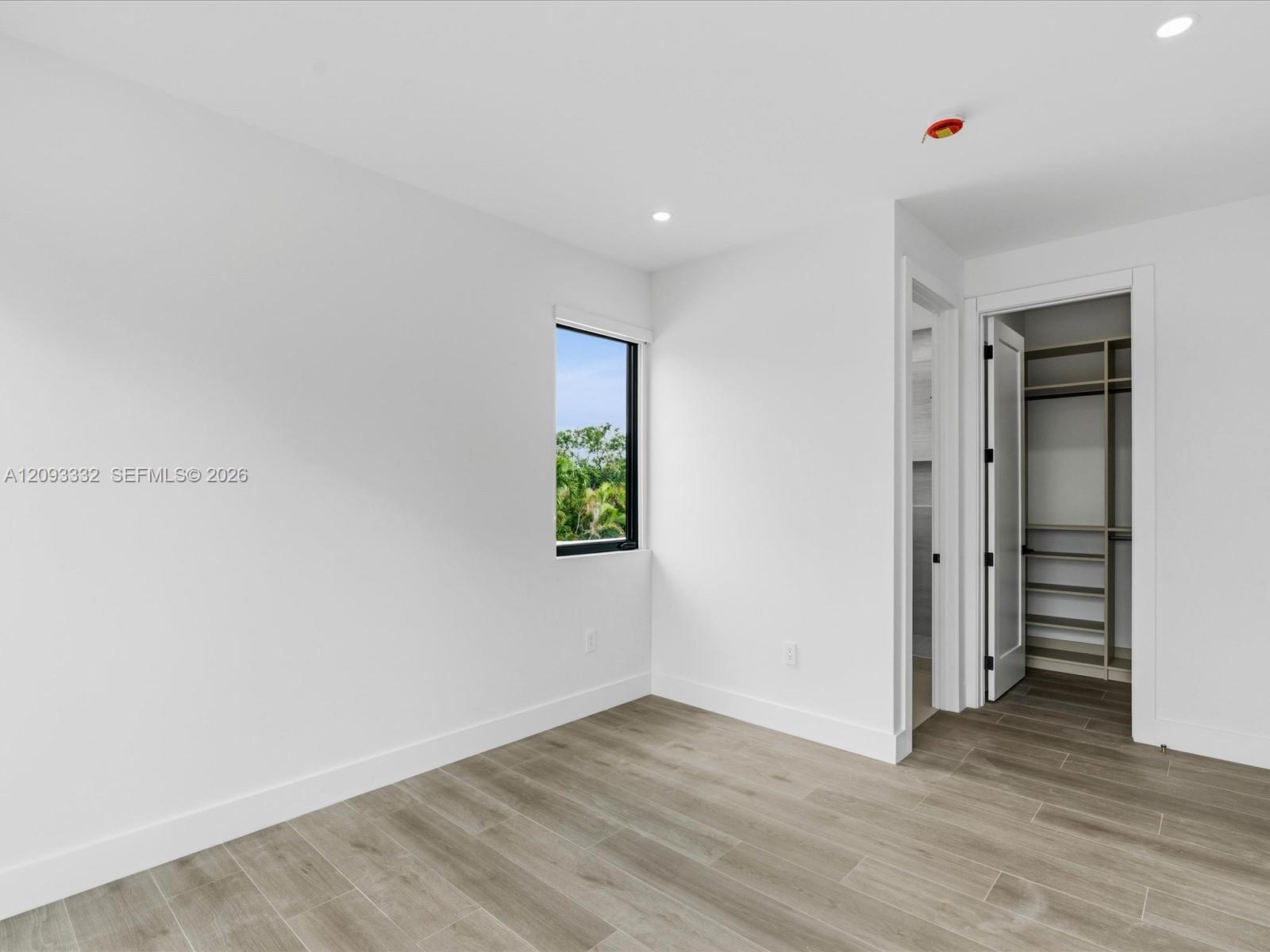 Neutral-toned interior featuring wood-finish flooring, recessed lighting, a single-pane black-trimmed window, and a walk-in closet with built-in shelv