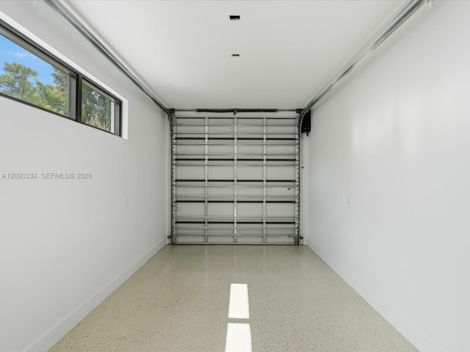 Finished garage featuring smooth white walls, high-gloss epoxy flooring, a horizontal window, and a metal roll-up door
