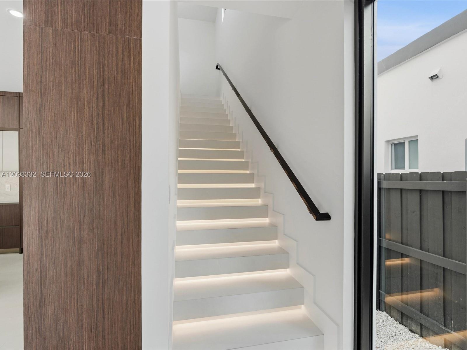 Staircase featuring illuminated risers, wood-finish wall paneling, and a minimalist black handrail