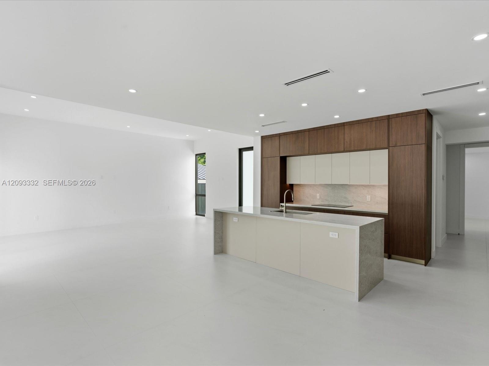 Modern kitchen featuring floor-to-ceiling cabinetry, a central island with stone-finish countertops, recessed lighting, and large-format tile flooring