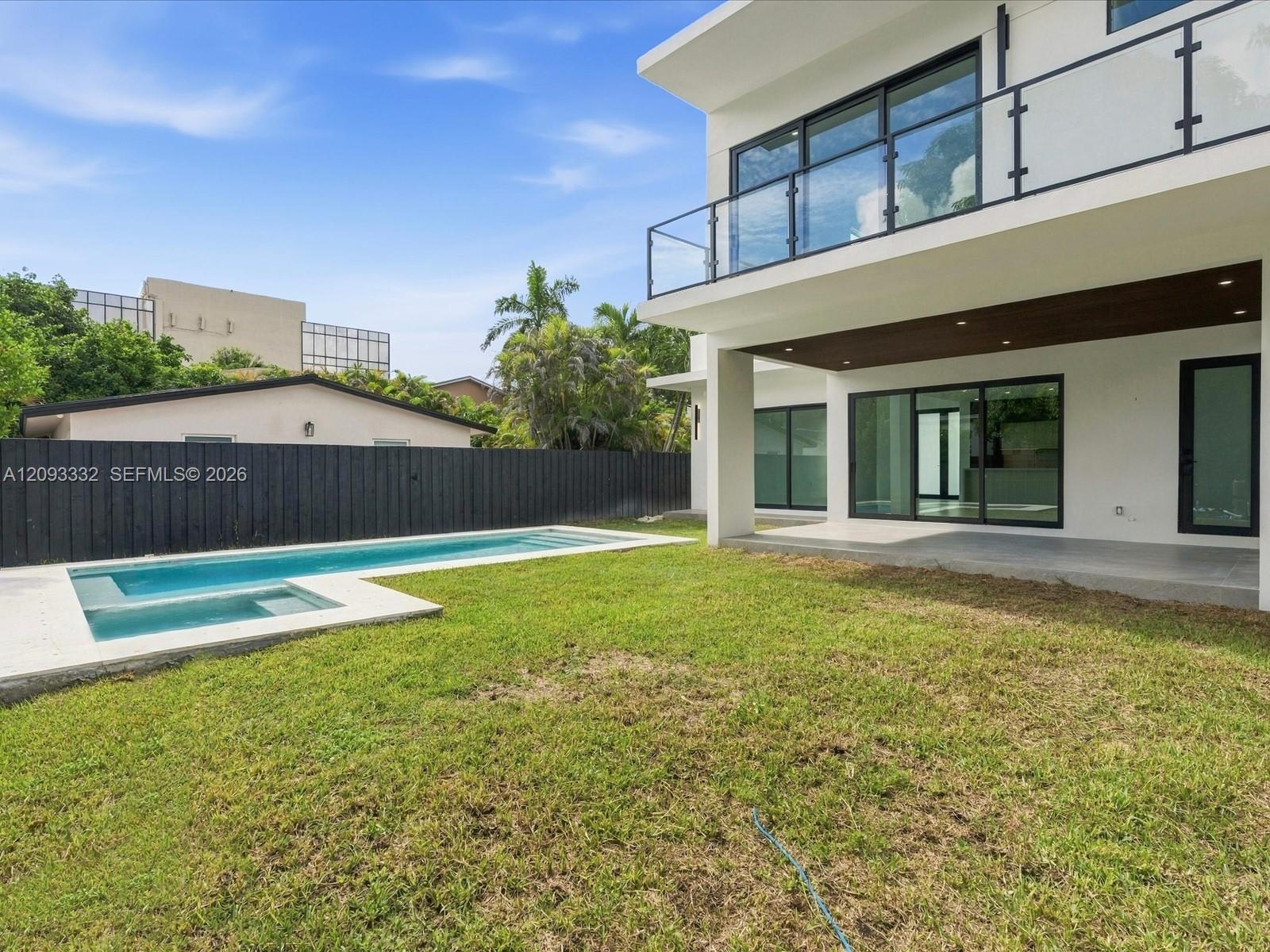 Modern architectural exterior featuring a second-story balcony with glass railings, a covered ground-level patio, an integrated swimming pool with a s
