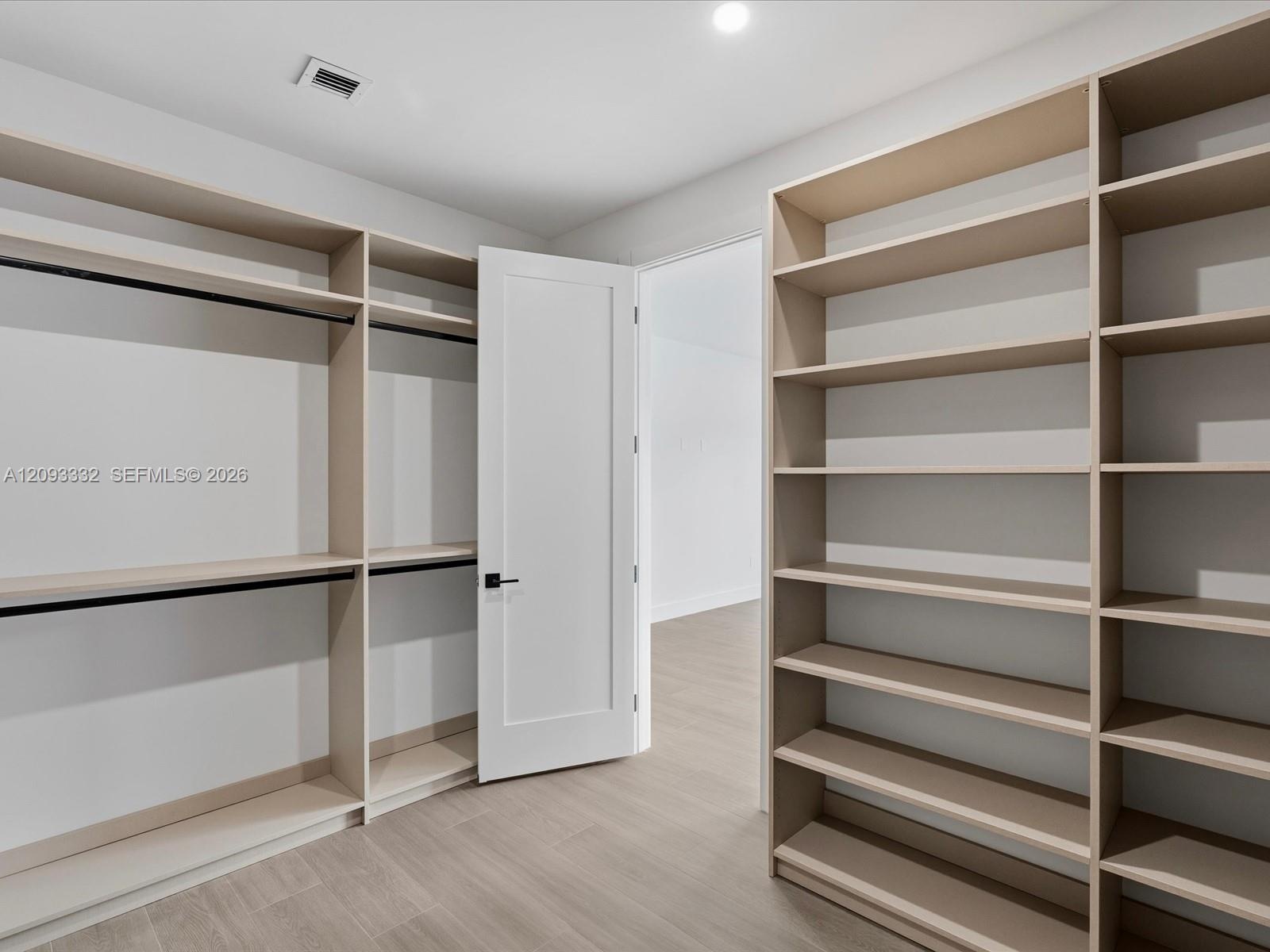 Custom-built cabinetry featuring expansive open shelving, integrated hanging rods, a shaker-style interior door, and neutral wood-finish flooring