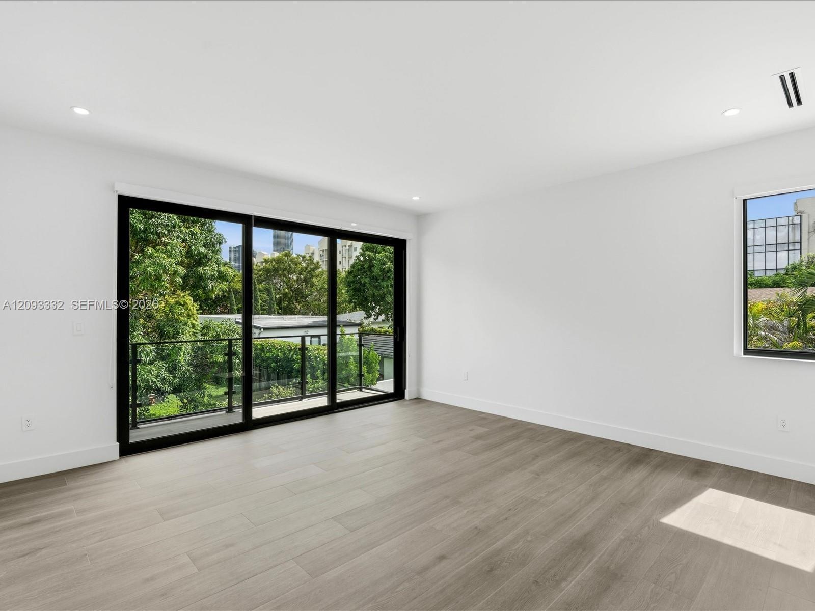 Interior space featuring wood-finish flooring, recessed lighting, and expansive floor-to-ceiling sliding glass doors opening to a balcony with a black
