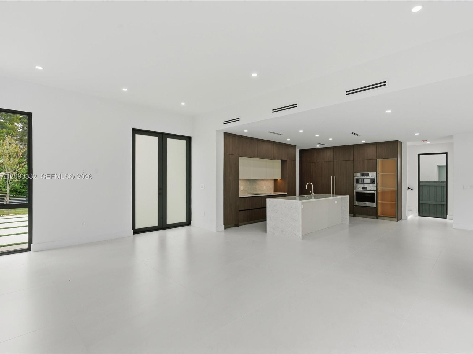 Open-concept interior featuring large-format tile flooring, a kitchen island with a stone-finish countertop, dark wood-finish cabinetry, built-in stai