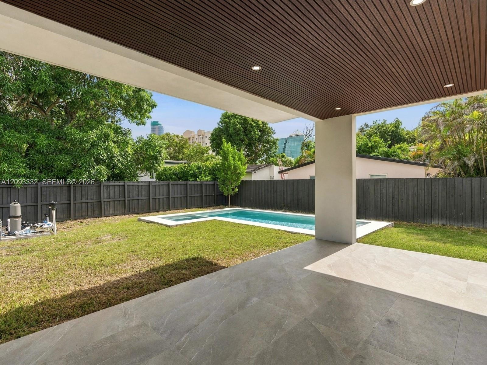 Covered outdoor patio featuring recessed lighting and wood-slat ceiling finish, complemented by a swimming pool with integrated spa and dark-tone priv