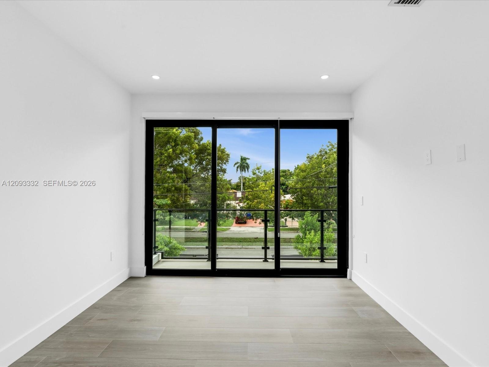 Multi-panel sliding glass doors with black frames, wood-finish flooring, recessed lighting, and a glass-paneled balcony railing
