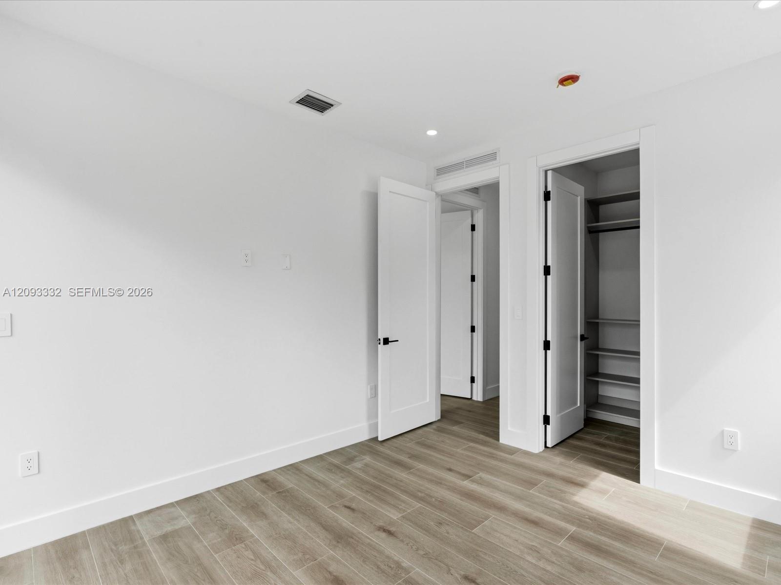Neutral-toned wood-finish flooring, crisp white walls, minimalist shaker-style interior doors with matte black hardware, and an integrated reach-in cl