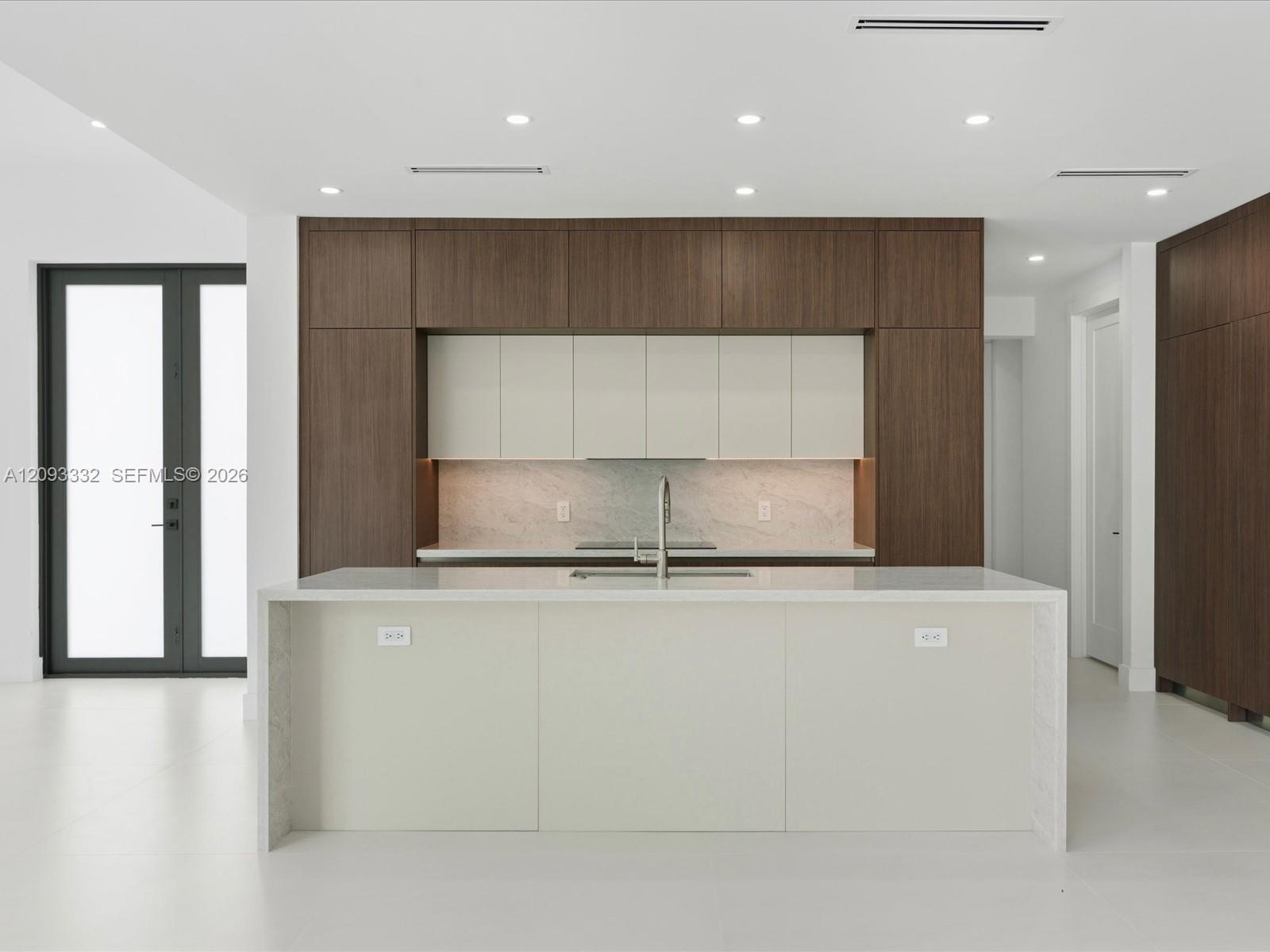 Contemporary kitchen featuring two-toned cabinetry, a waterfall-edge center island, solid-surface countertops, stone-finish backsplash, and recessed c