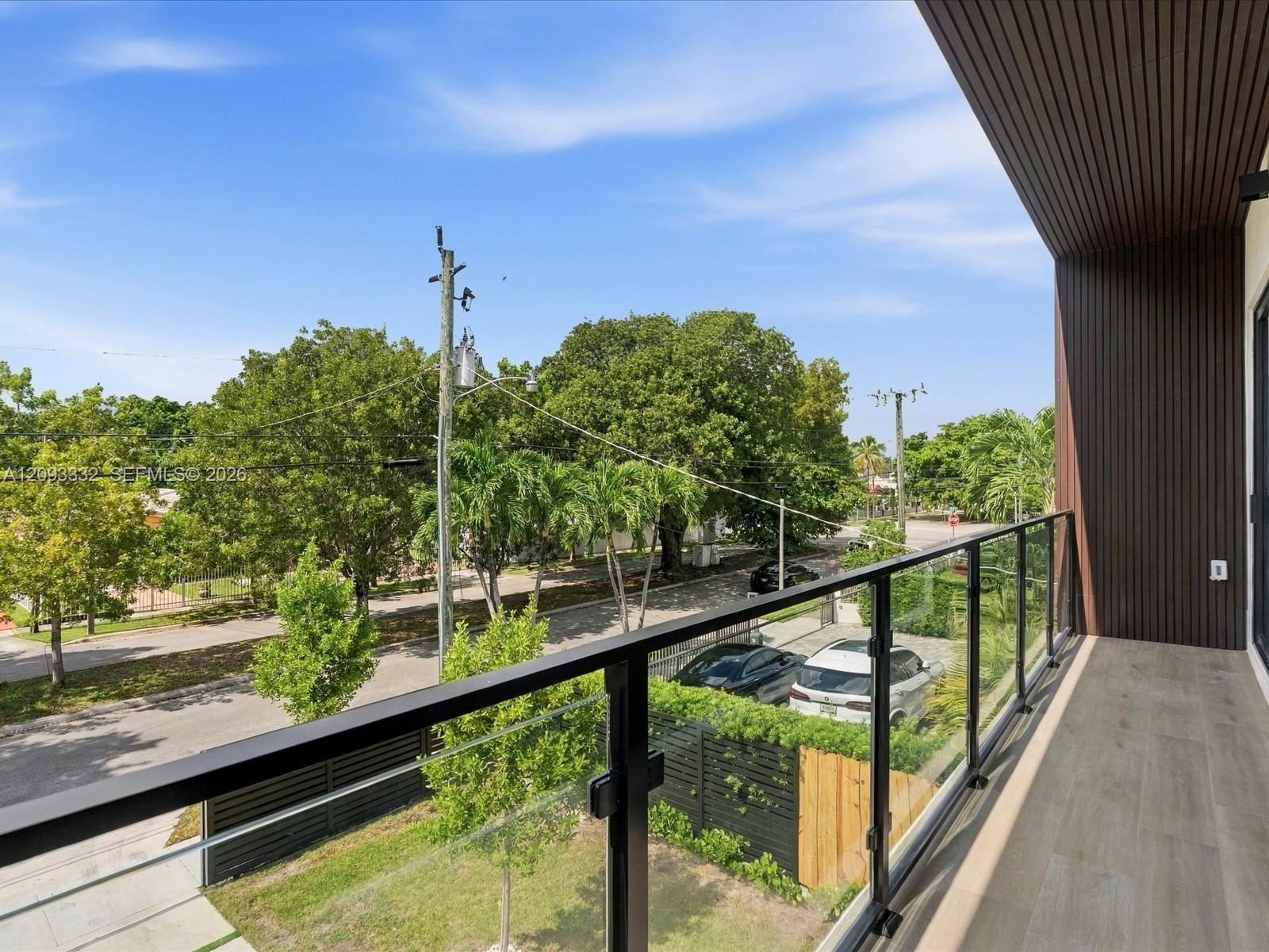 Covered balcony featuring wood-finish ceiling paneling, light-tone flooring, and a glass panel railing with a black metal frame