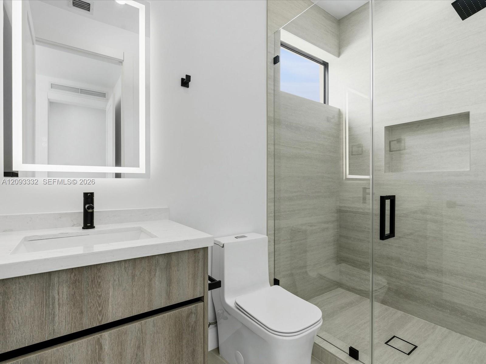 Floating vanity with a light wood-finish cabinetry, rectangular integrated sink, illuminated LED mirror, and matte black hardware