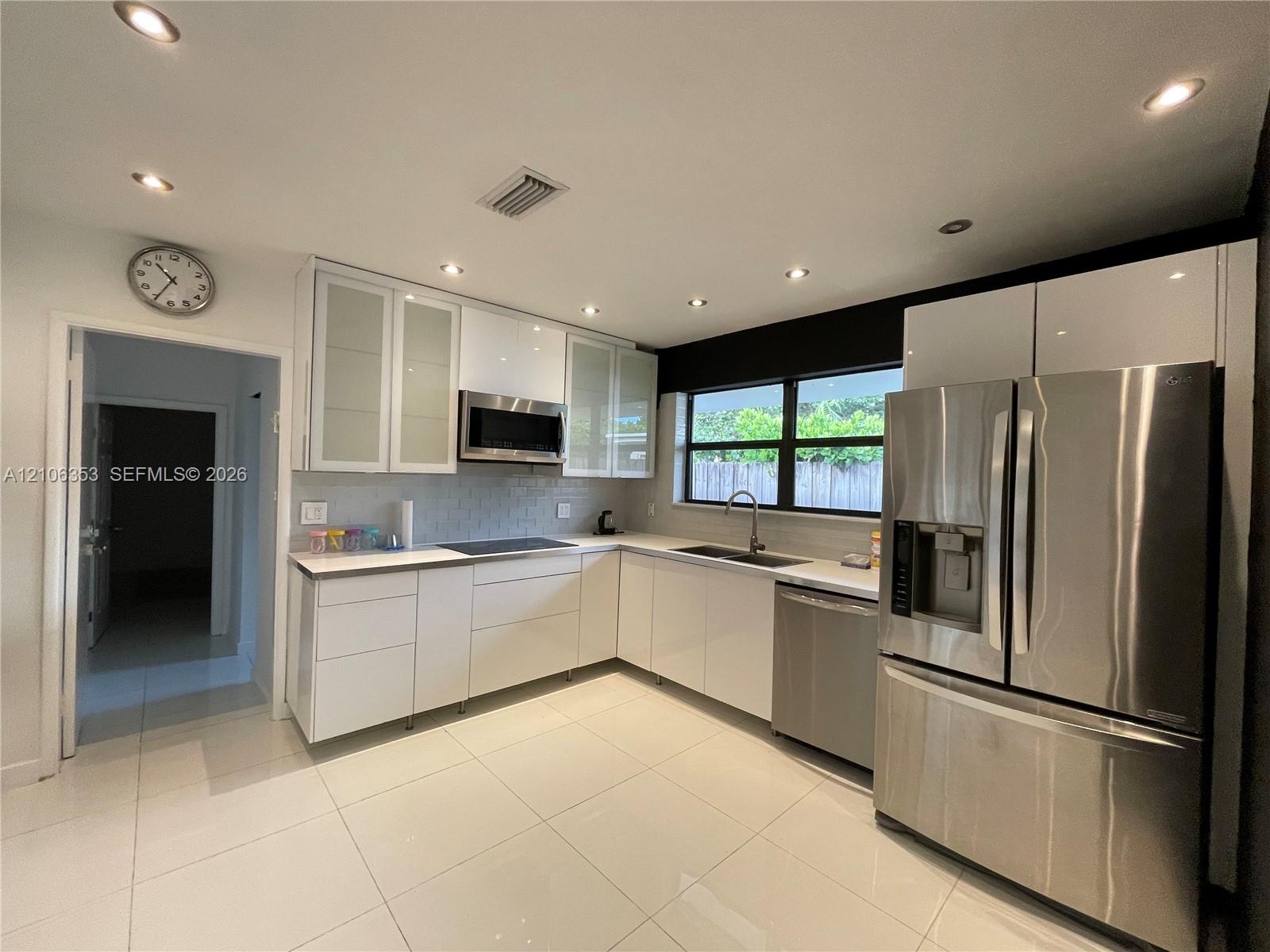 Modern kitchen featuring flat-panel white cabinetry, stainless steel appliances, recessed ceiling lighting, light-toned tile flooring, and a subway-st