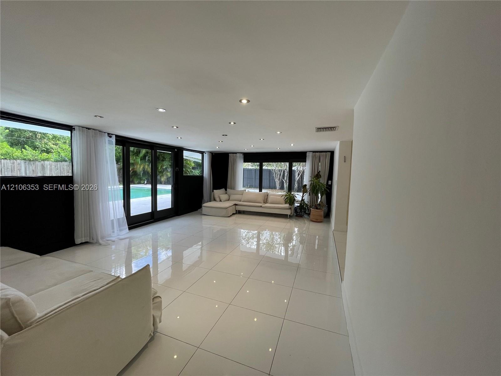 Expansive living area featuring large-format tile flooring, recessed ceiling lighting, and floor-to-ceiling glass sliding doors opening to an outdoor 