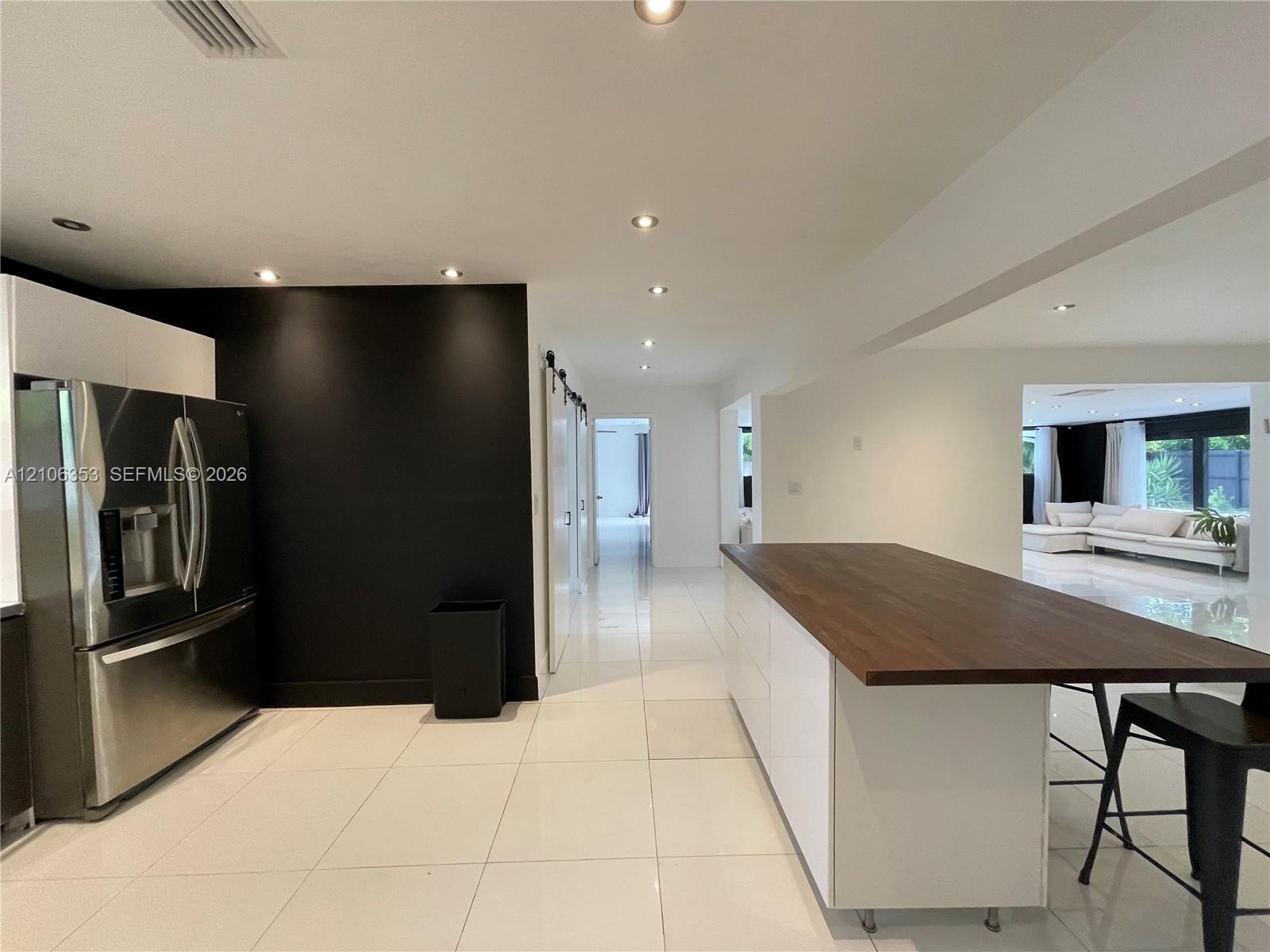 Kitchen featuring a white cabinetry island with a wood-finish countertop, high-gloss large-format tile flooring, stainless steel refrigerator, and rec