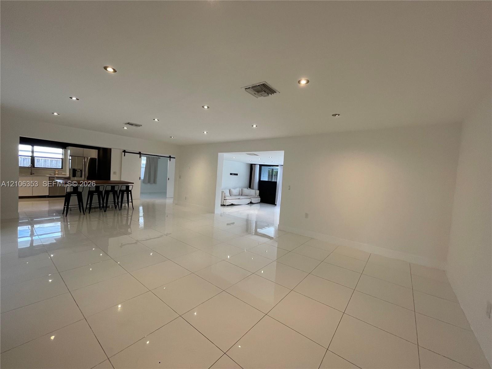 Large-format ceramic tile flooring, recessed ceiling lighting, kitchen island with breakfast bar seating, and sliding barn-style door