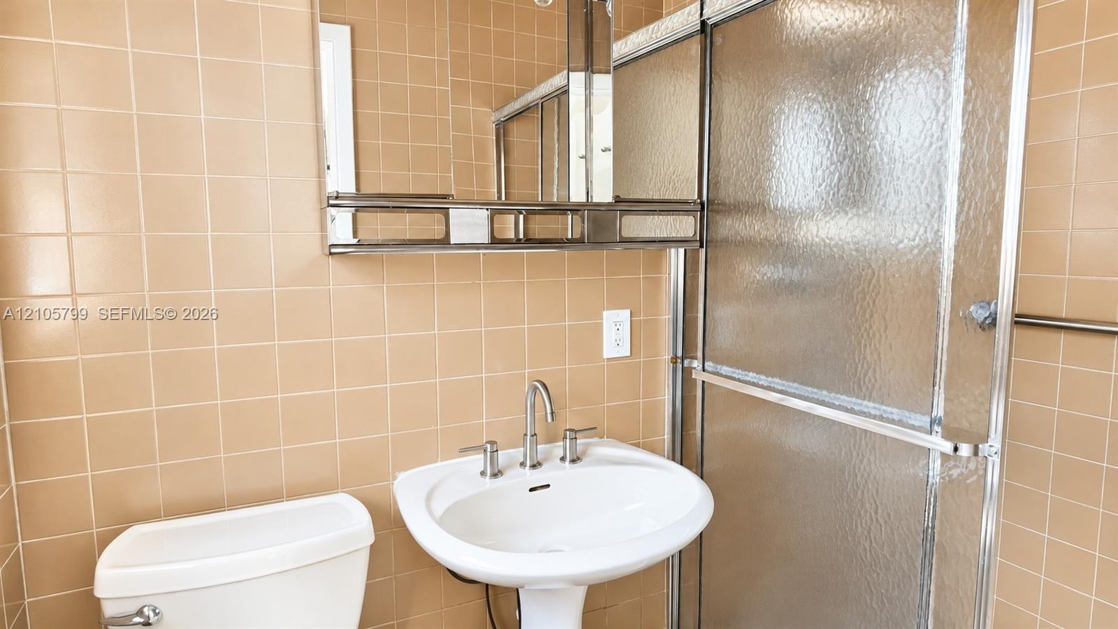 Wall-mounted medicine cabinet with integrated shelving, pedestal sink, metallic widespread faucet, and shower enclosure with textured glass doors, set