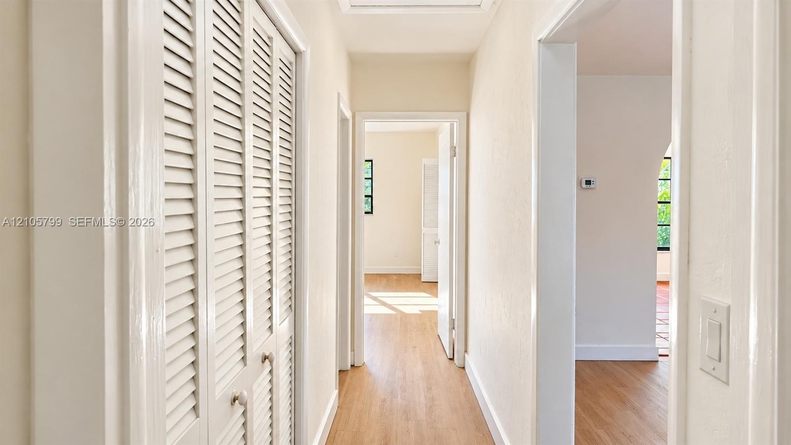 Hallway featuring wood-finish flooring, white louvered-door closets, and arched doorways