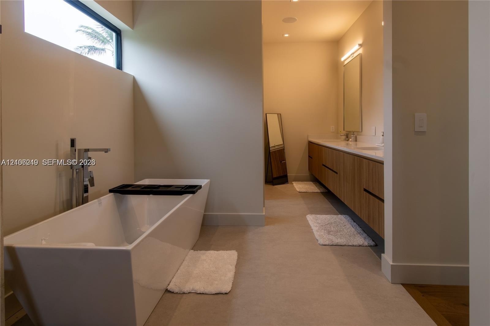 Freestanding soaking tub with floor-mounted faucet, horizontal clerestory window, dual-sink vanity with wood-finish cabinetry, and neutral large-forma