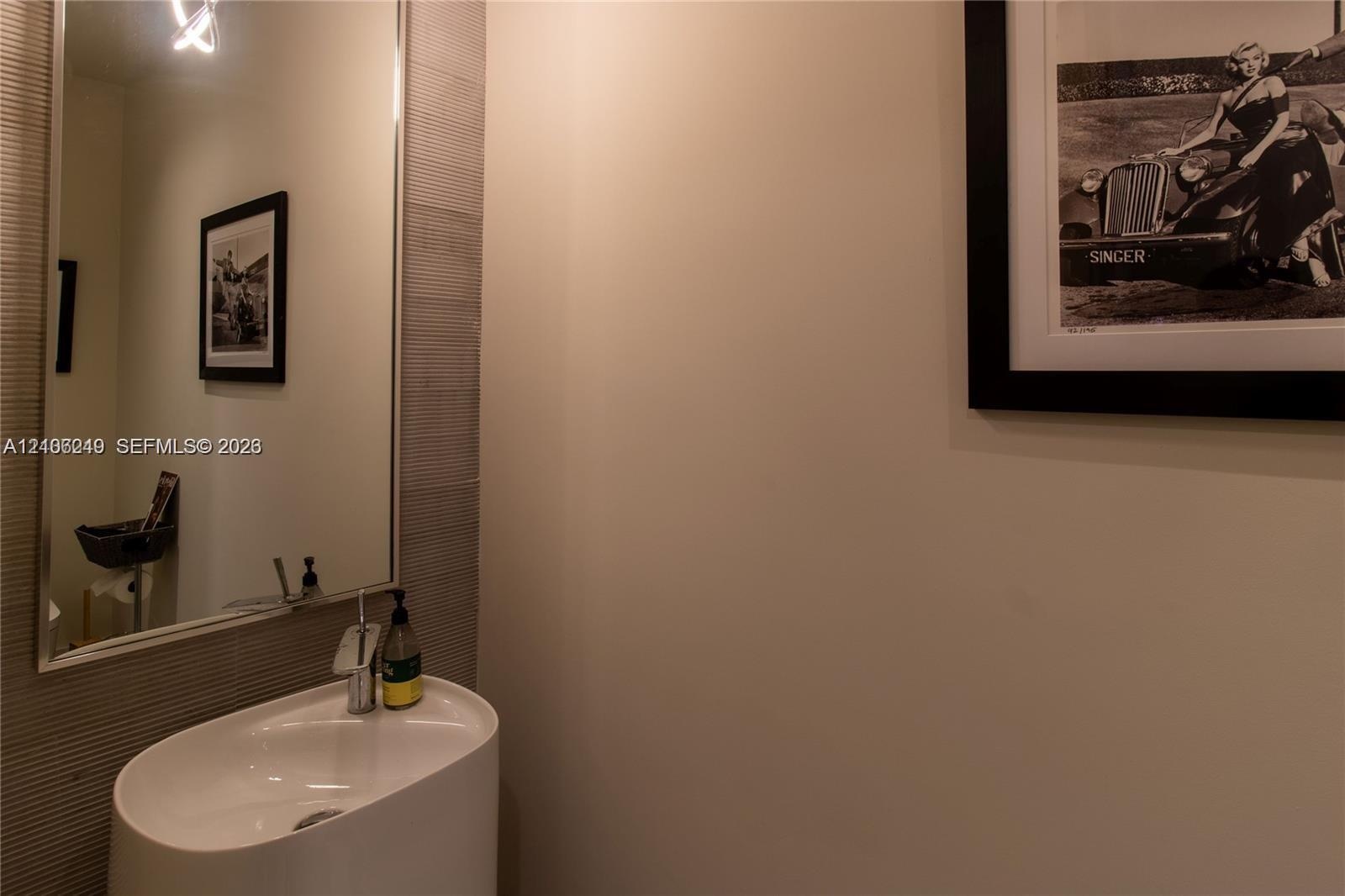 Modern powder room featuring a streamlined oval vessel sink, chrome single-handle faucet, oversized rectangular wall mirror, and textured tile wall ac